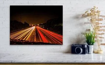 Long exposure night photograph of red and gold light trails on Interstate 64 in St. Louis, converging toward an overpass under a black sky
