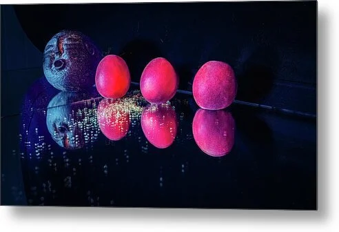 Carried on the Wind – fine art still life photograph of three apricots and a carved stone face lit in warm and cool tones on a reflective black surface
