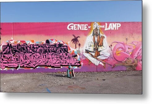 Long magenta-to-peach mural wall in St. Louis with pink graffiti lettering at left, silhouetted palm trees, a seated white-robed figure under the words Genie of the Lamp and a brown lamp at right