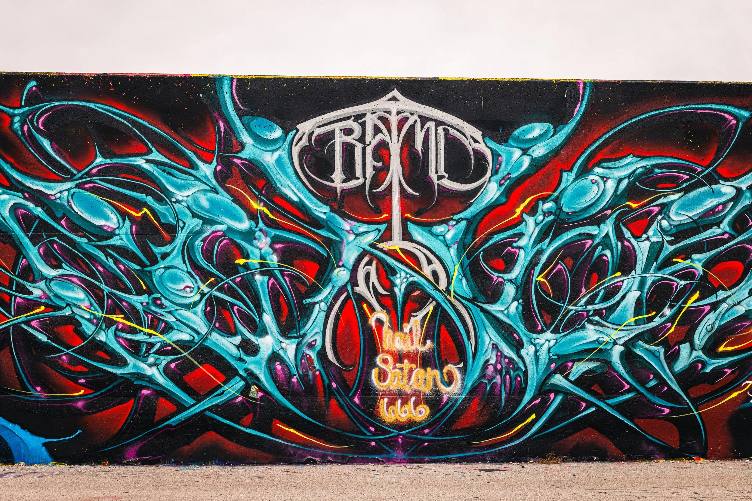 Colorful graffiti mural on a wall with abstract designs in shades of blue, red, purple, and black, featuring a central white emblem with the text 'RMS' and additional smaller text below it.