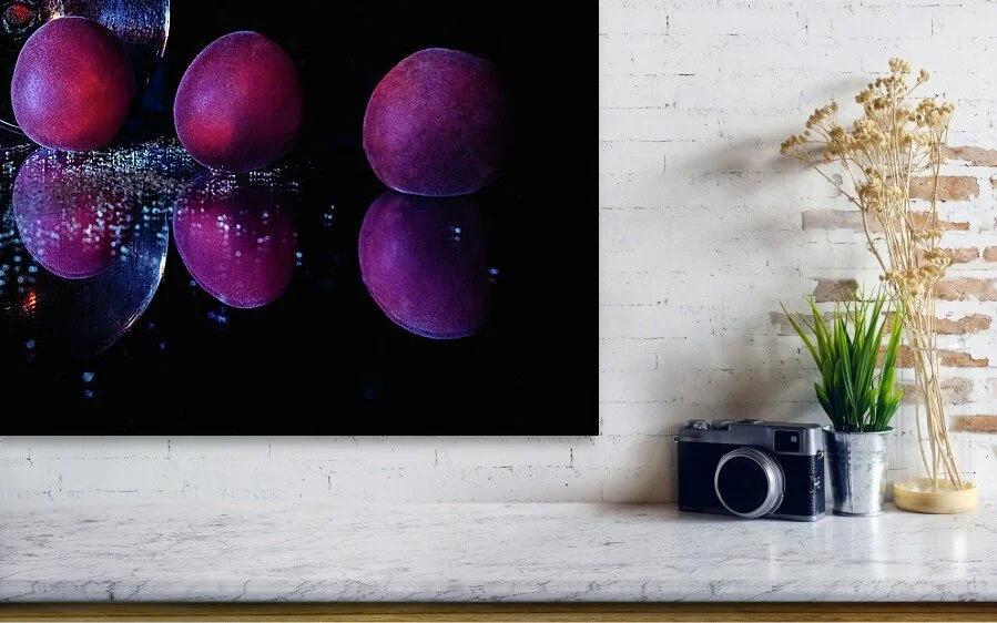 Three Plums, After Dark, close-up detail of the fine art print above a marble ledge with a camera and a plant