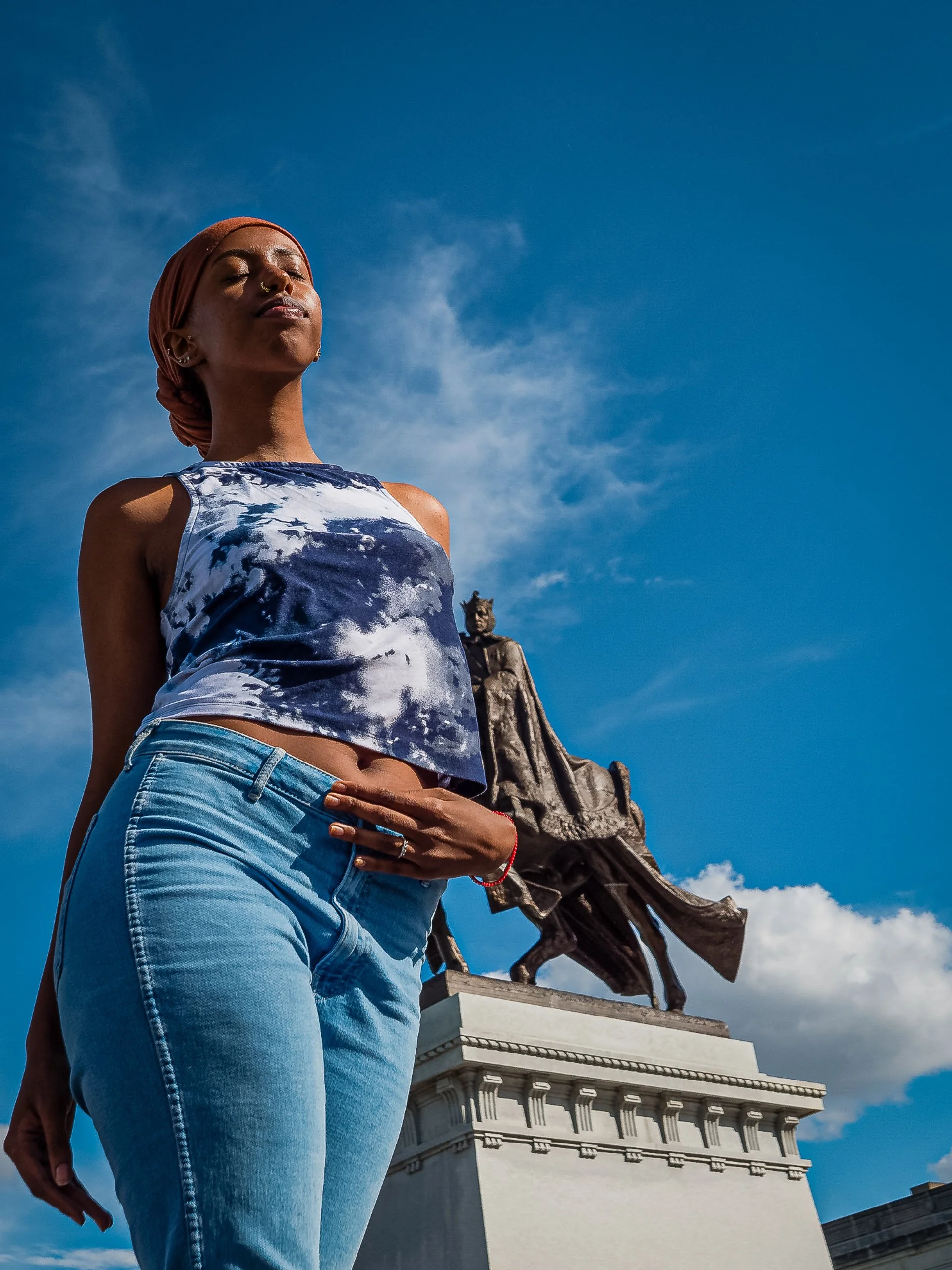 Low-angle color portrait of a young woman standing beneath a blue sky with the Apotheosis of St. Louis statue of King Louis IX behind her at the Saint Louis Art Museum in Forest Park.