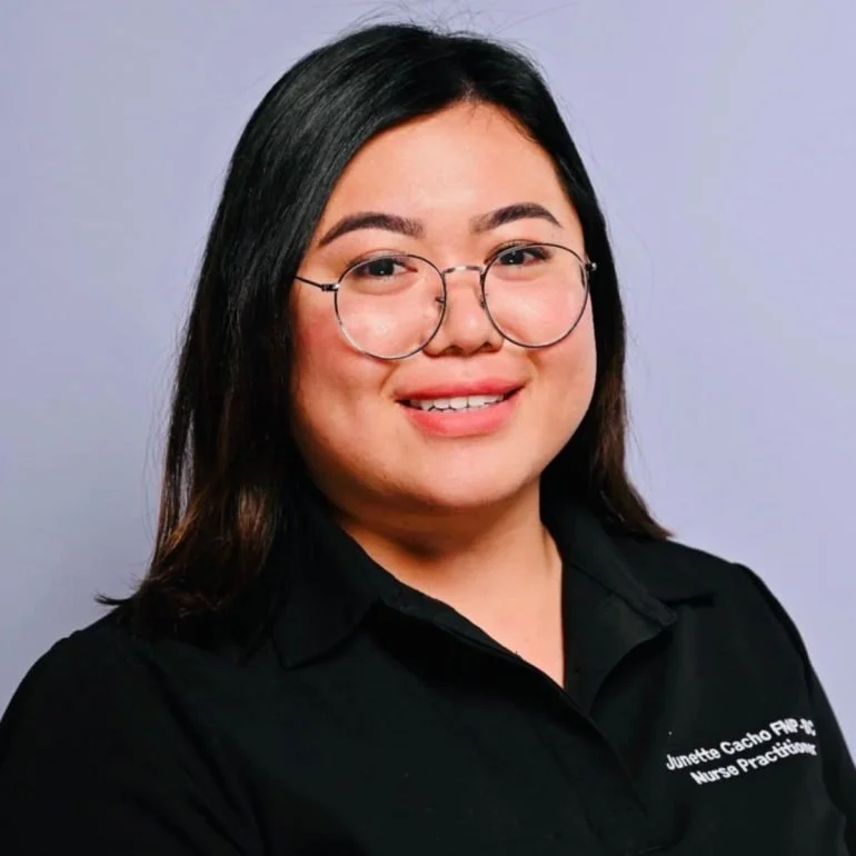 A woman with shoulder-length dark hair and glasses, wearing a black collared shirt, smiles at the camera against a plain background.