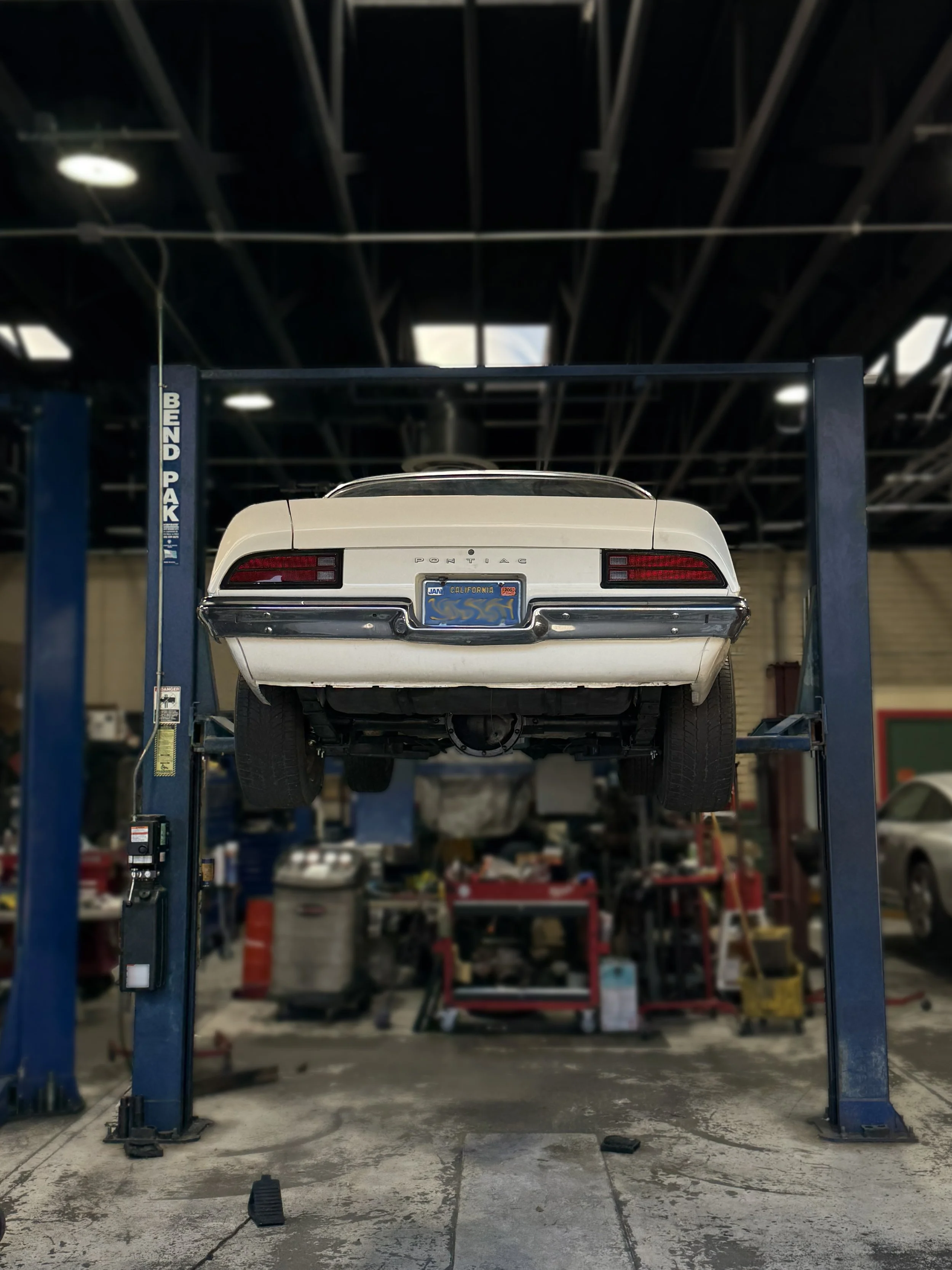 A white Pontiac car is lifted on a blue hydraulic vehicle lift in a garage or auto repair shop.