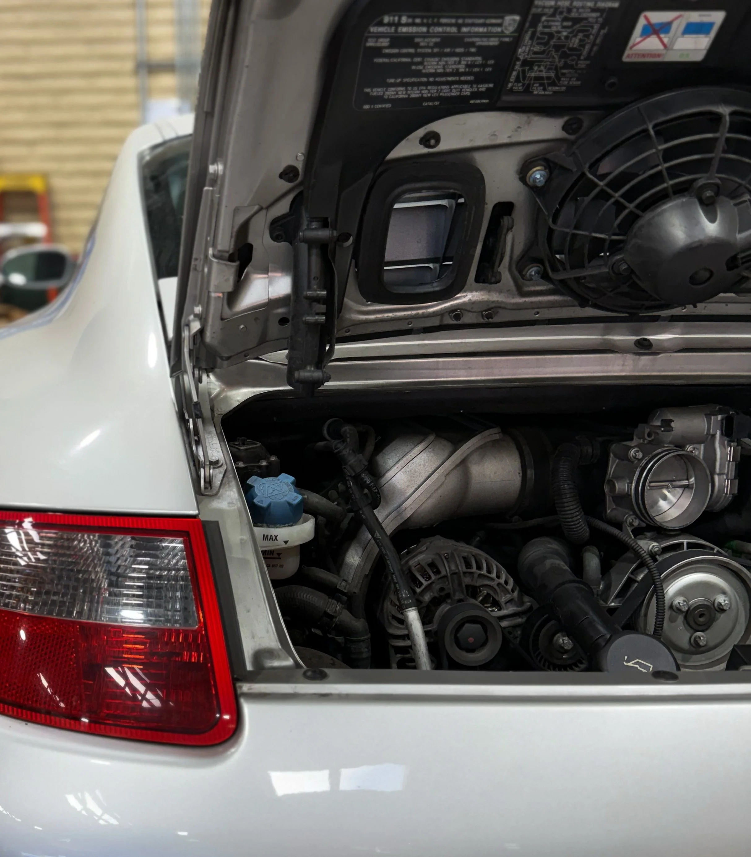 Rear corner of a white car with the trunk open, revealing the engine compartment.