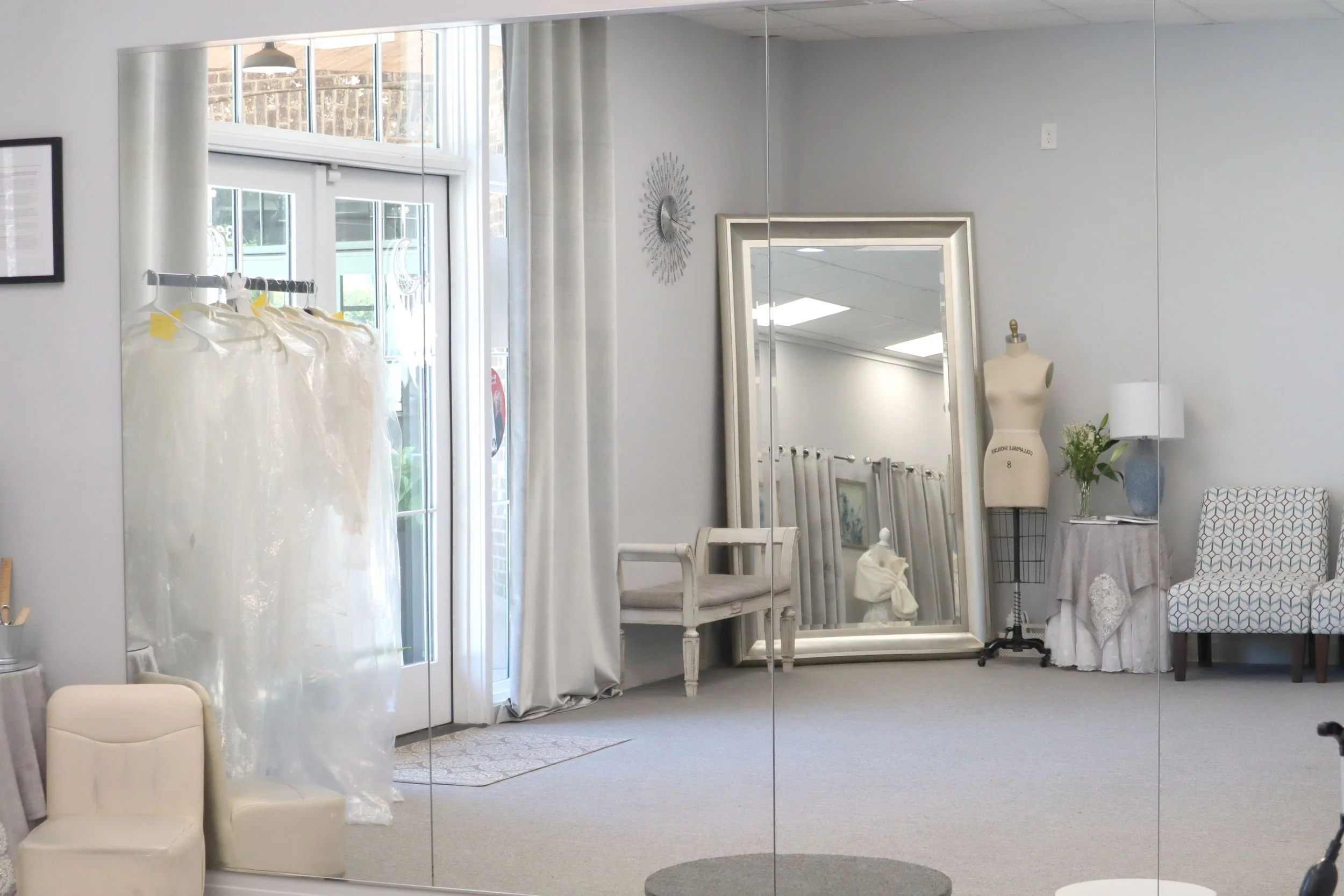 Interior of a furniture or decor store with a large mirror, white chairs, a mannequin, a table with a lamp, and decorative items.