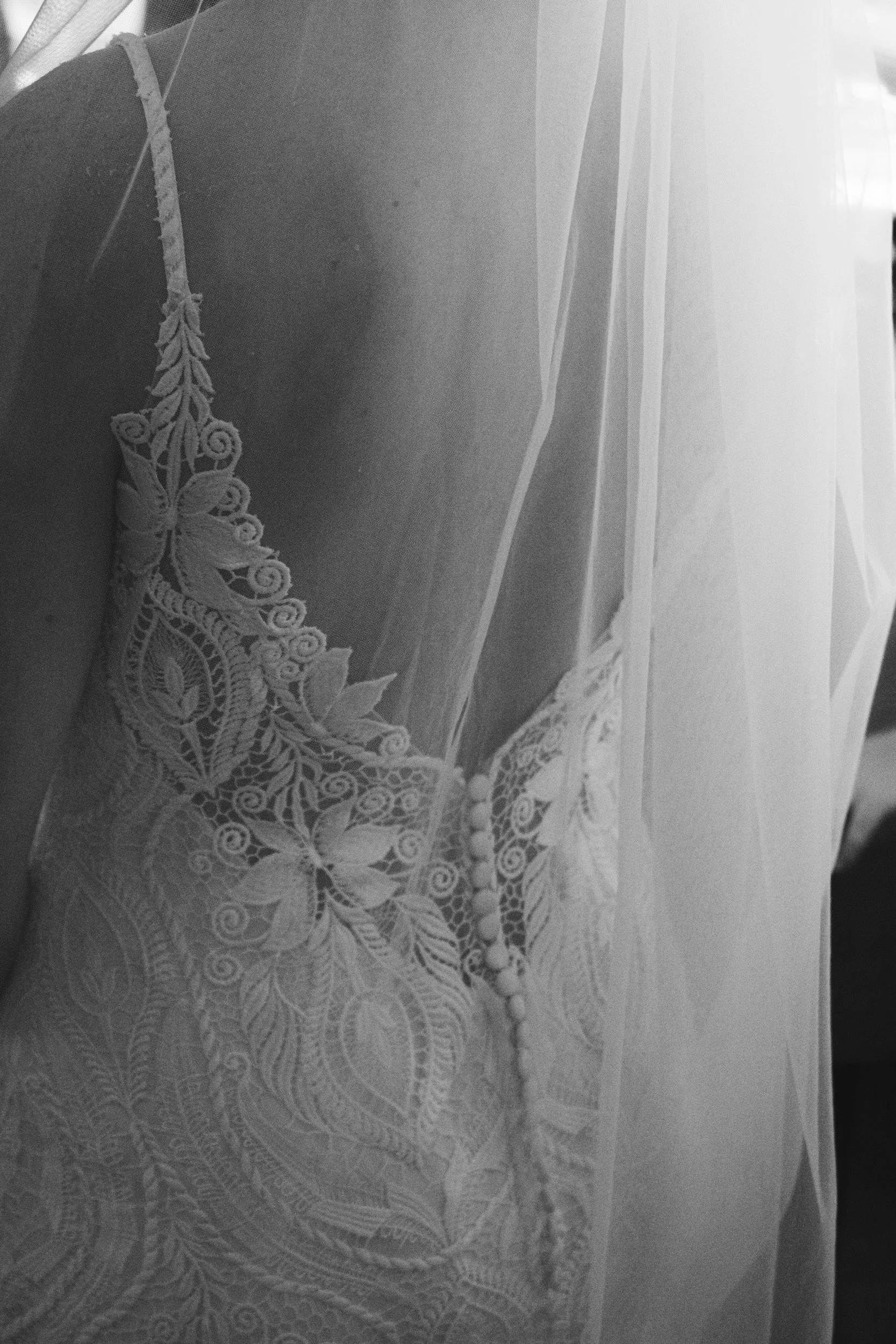 Close-up of a lace wedding dress with intricate floral embroidery and a row of buttons.
