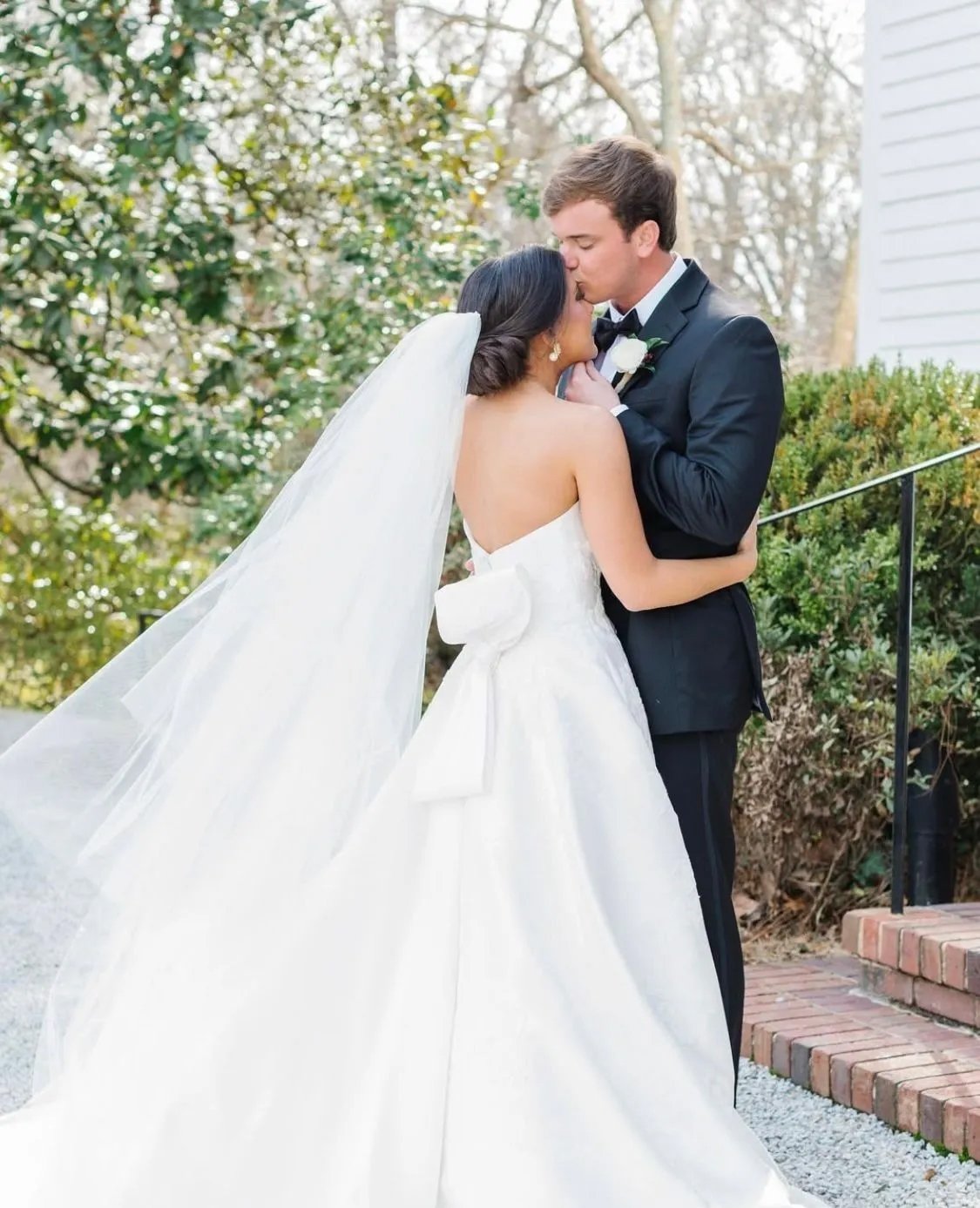 A bride and groom sharing a kiss outdoors on a wedding day.