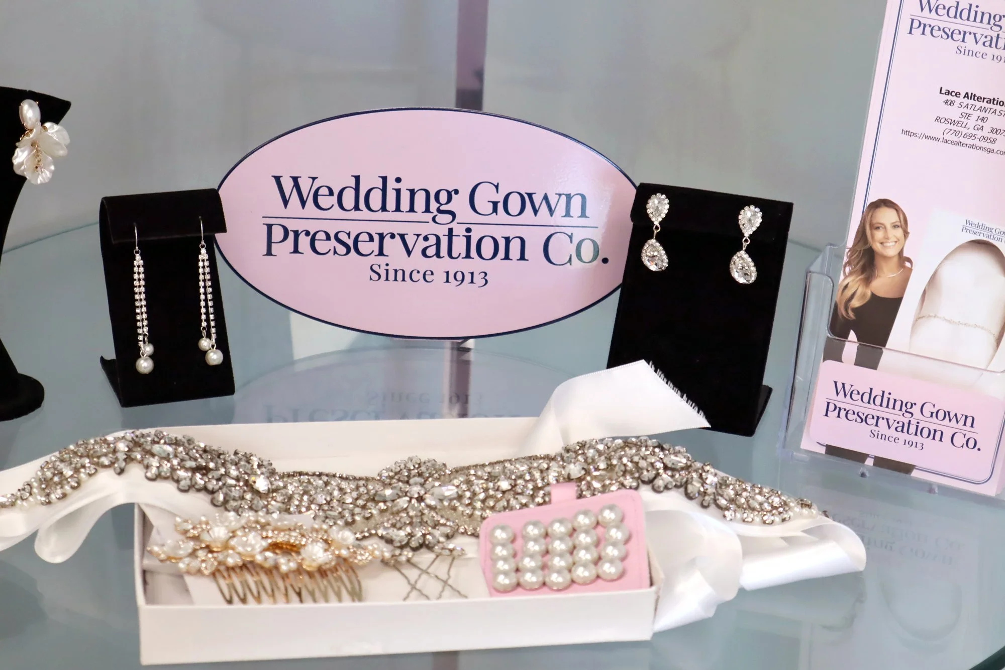 Display of jewelry including pearl and crystal earrings, pearl hairpins, and a pearl bracelet, with a sign for Wedding Gown Preservation Co.