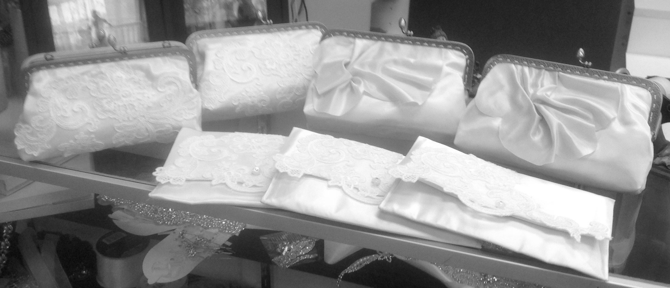 A display of clutch purses with white embroidered and satin patterns, arranged on a glass table.