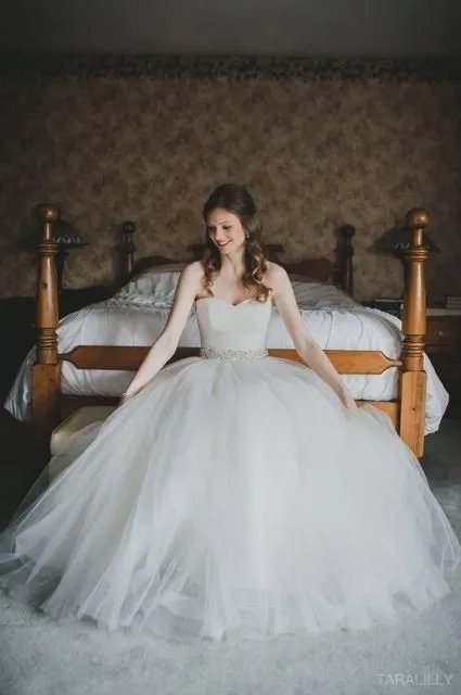 Young woman in a wedding dress sitting on a bed in a bedroom.