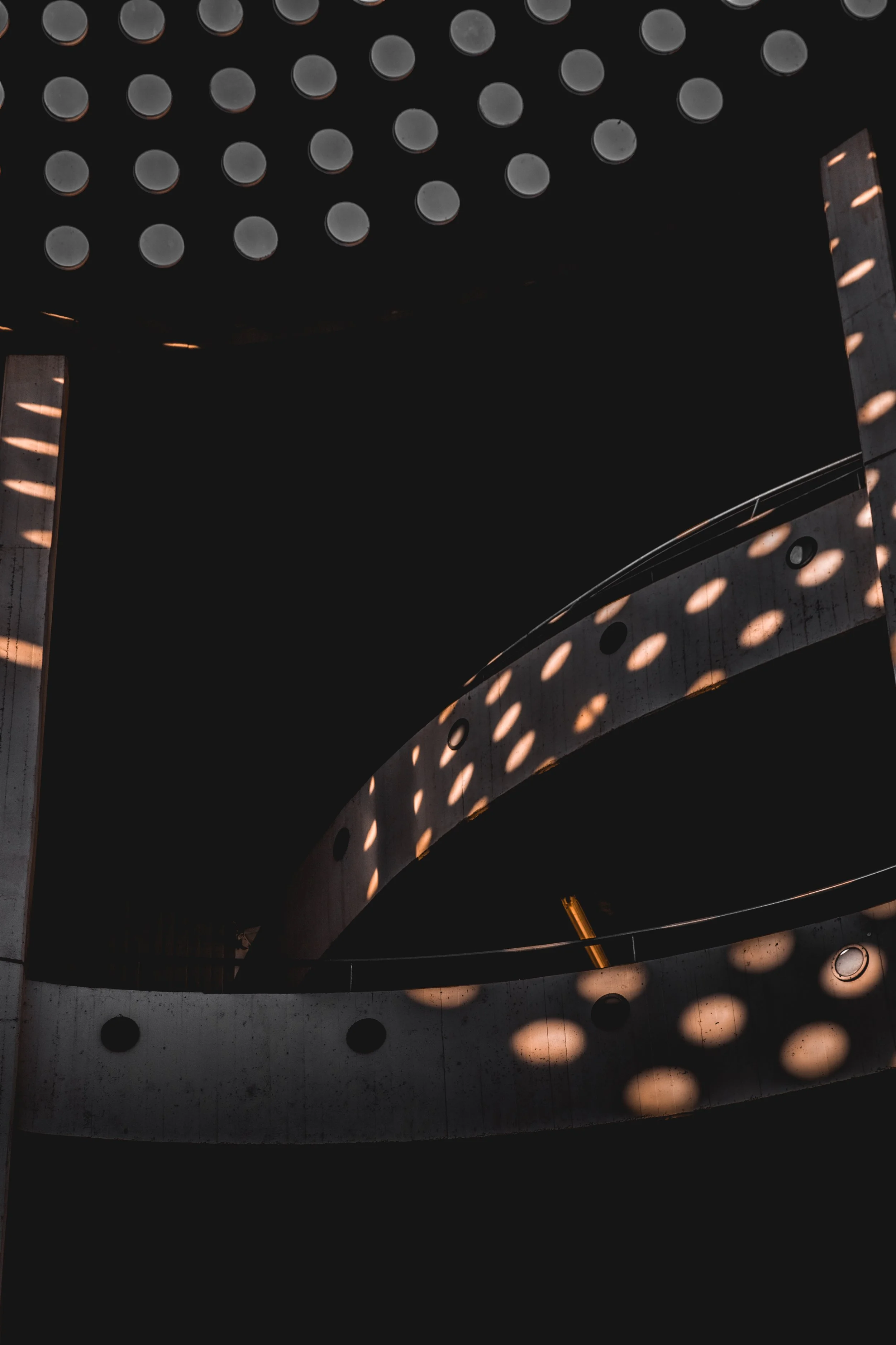 Interior view of a modern building with distinctive architectural design featuring circular cut-outs and curved concrete walls, illuminated by light coming through the circular openings creating patterns of light and shadow.