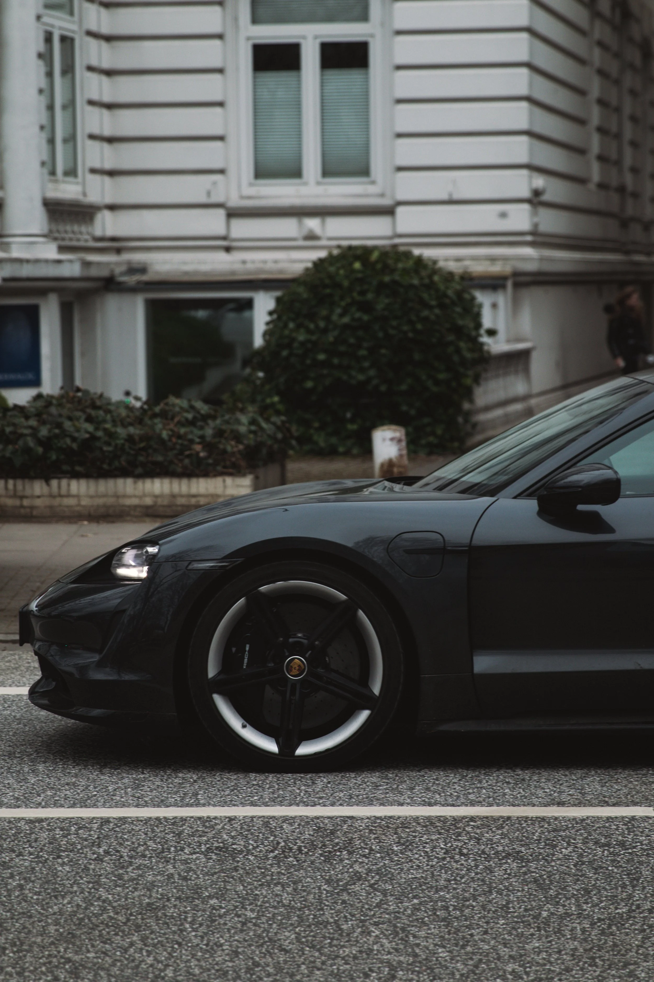 Close-up of a black luxury sports car parked on a street, with a building and landscaping in the background.