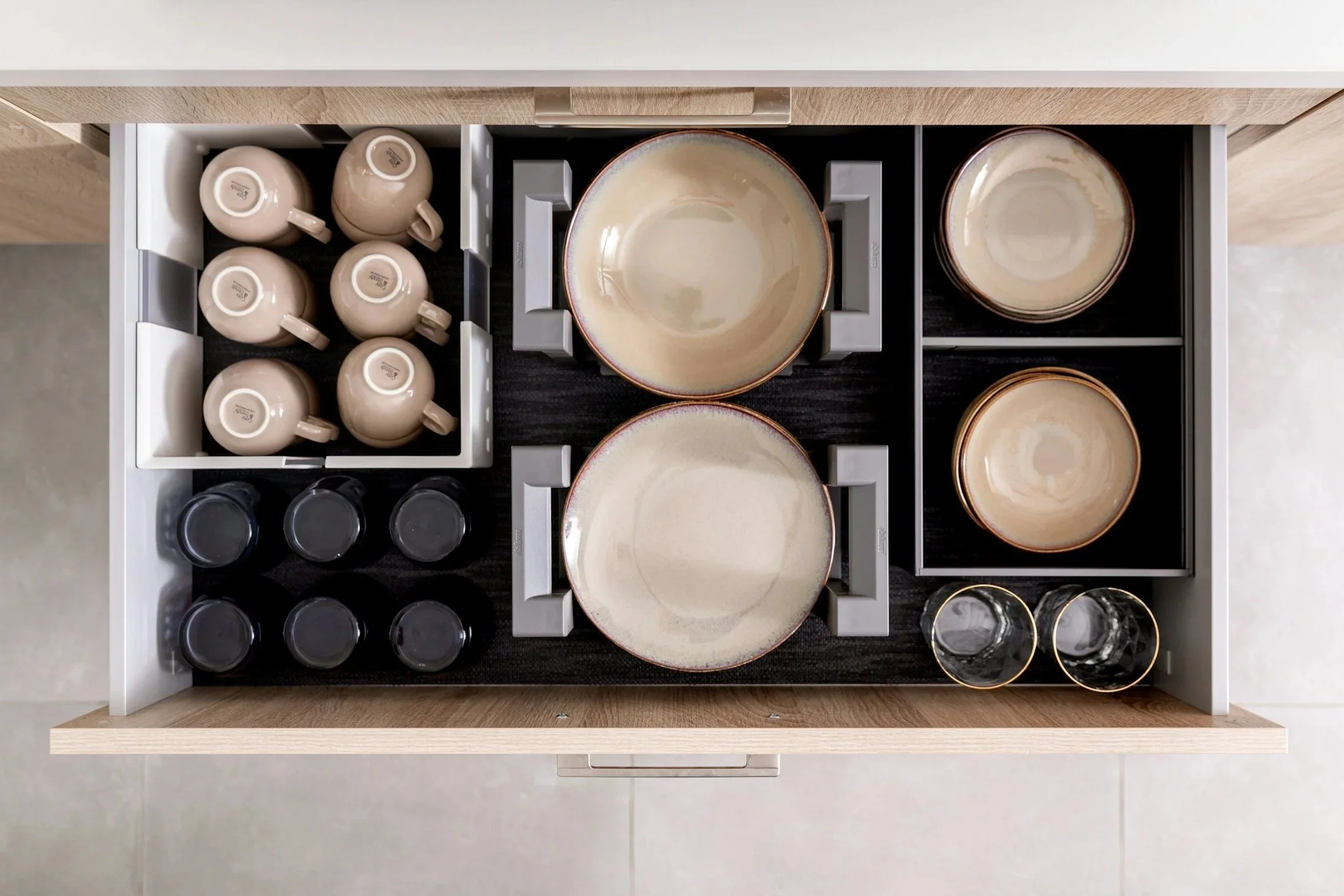 Open drawer containing neatly organized beige coffee mugs, plates, and small bowls.