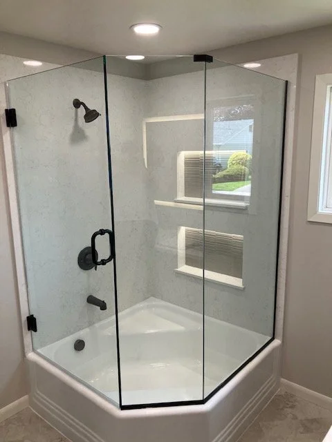 A modern shower with a glass enclosure, black fixtures, and built-in wall shelves, in a bright bathroom with a window.