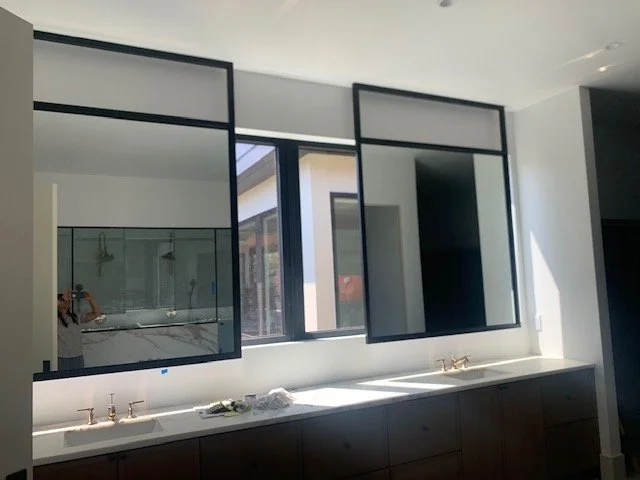Modern bathroom with large window, double vanity, and mirrors above sinks.