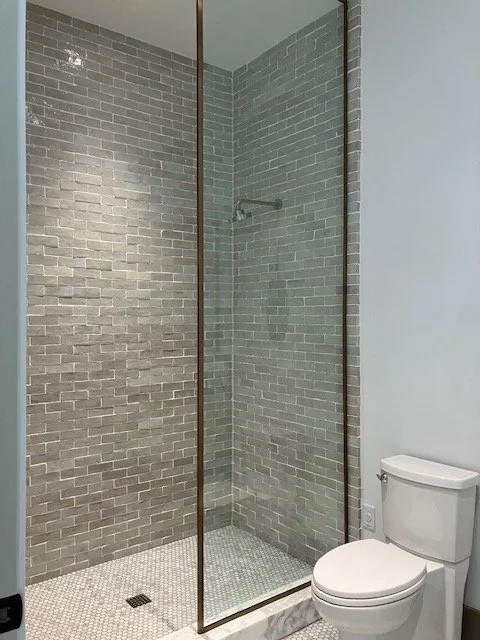 Modern walk-in shower with gray brick tiles, glass enclosure, and a white toilet nearby.