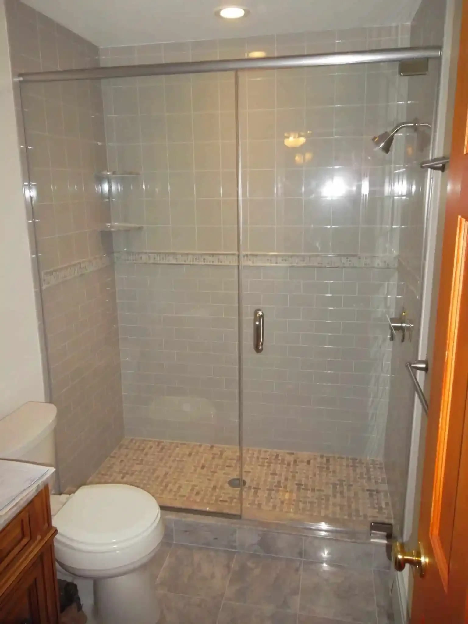 Bathroom with a glass shower enclosure, a toilet, tiled walls, and a wooden door.