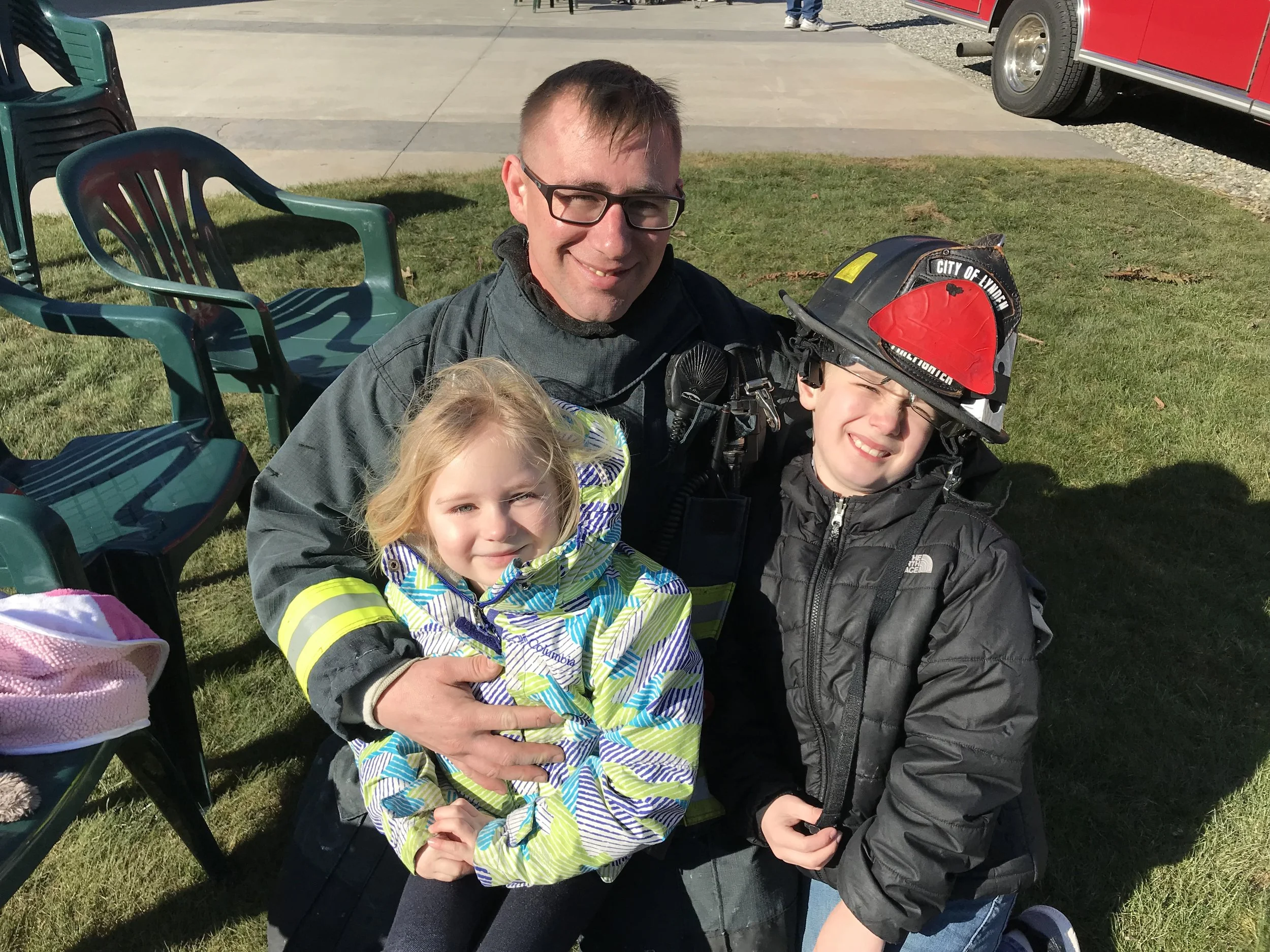 A firefighter in bunker gear with two kids smiling