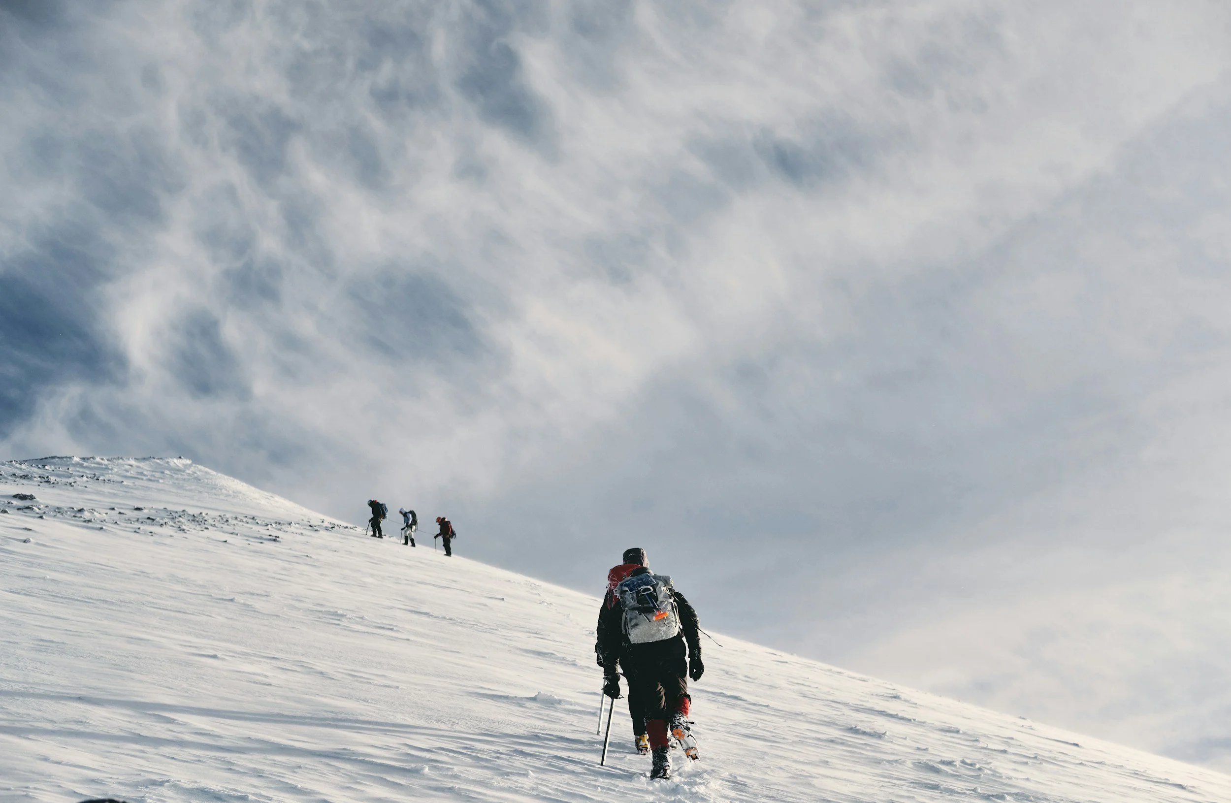 Personas haciendo esquí de fondo en un paisaje nevado con cielo nublado.