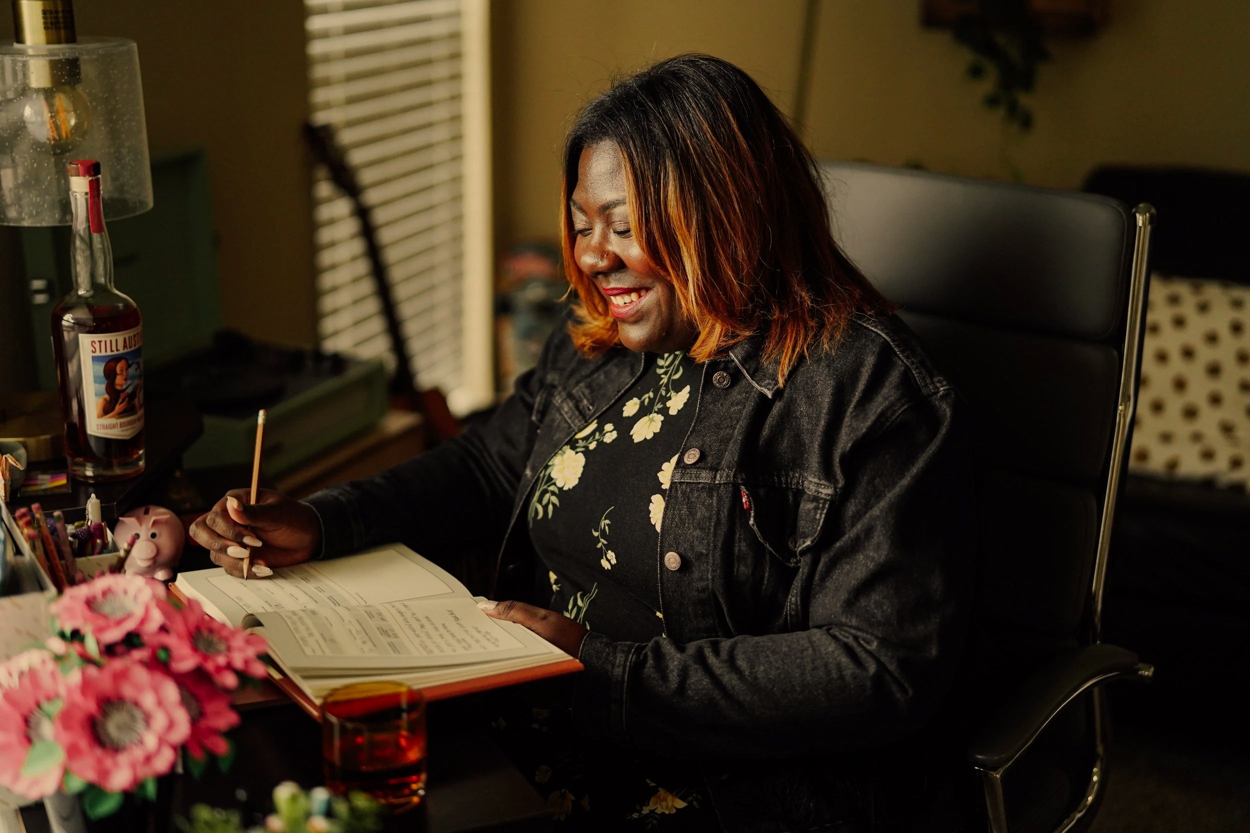 Gabrielle Nicole Pharms writing at a desk in a warmly lit workspace.