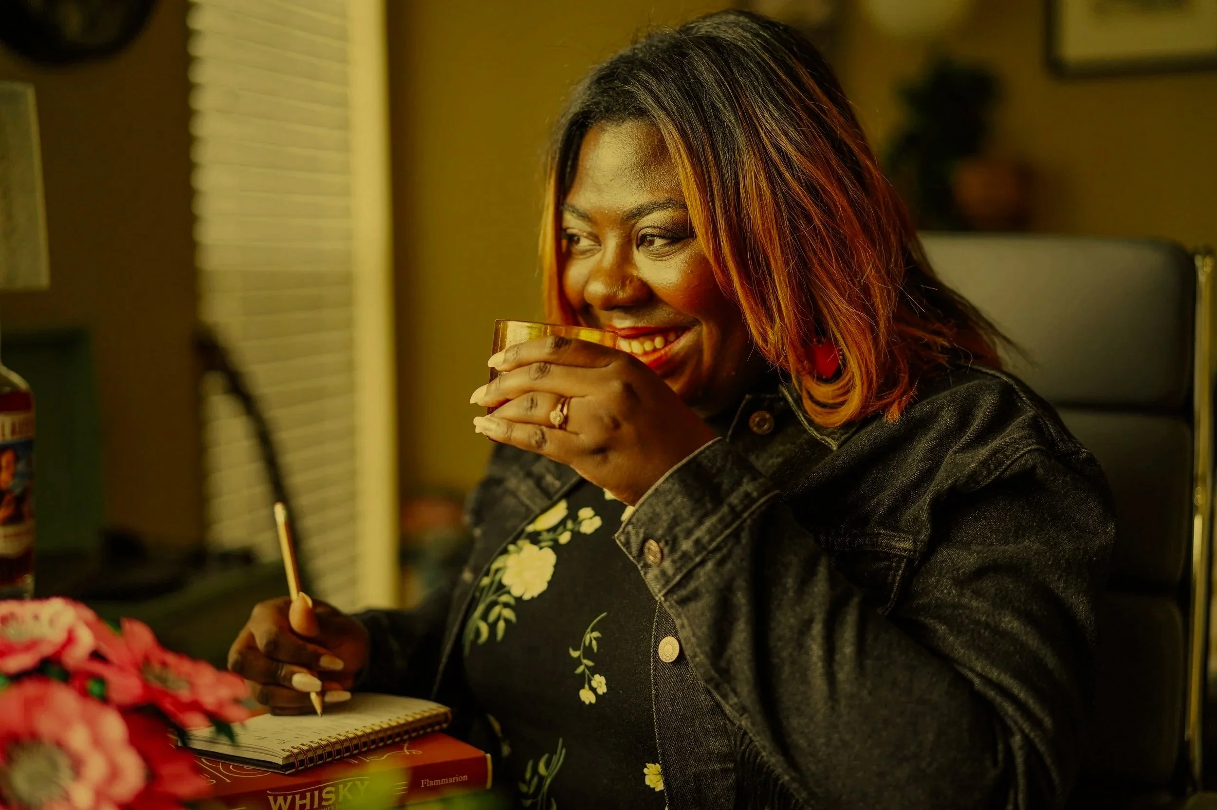 Gabrielle Nicole Pharms smiling while nosing a whiskey and making tasting notes in a creative workspace.