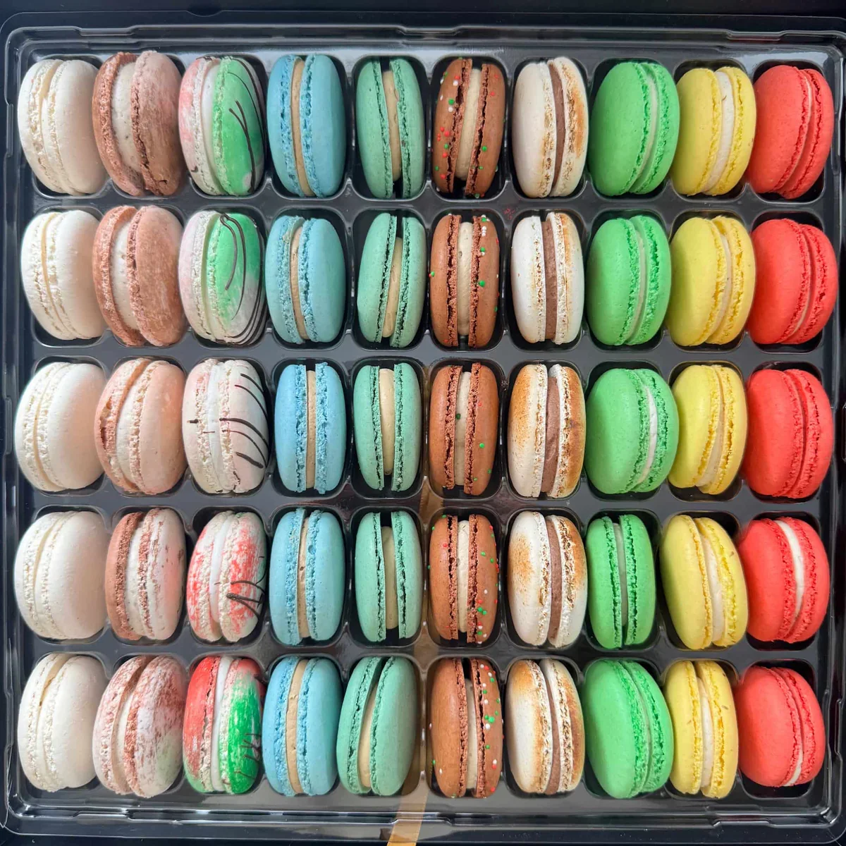 A tray of 36 colorful macarons in assorted pastel and bright colors, arranged in six rows of six.
