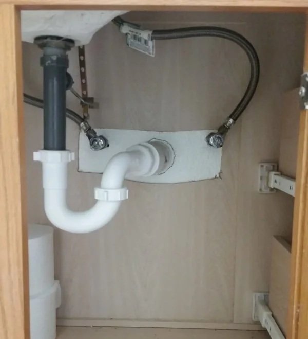 An open bathroom cabinet showing the pipes under the sink
