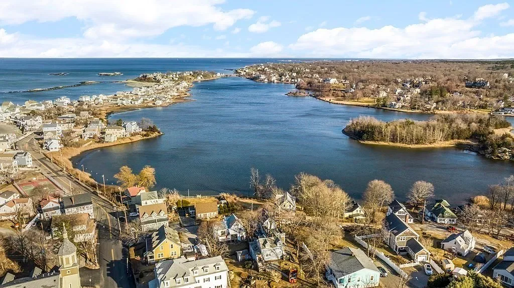 Aerial view of a residential neighborhood around a large lake with houses, trees, and the ocean in the distance.