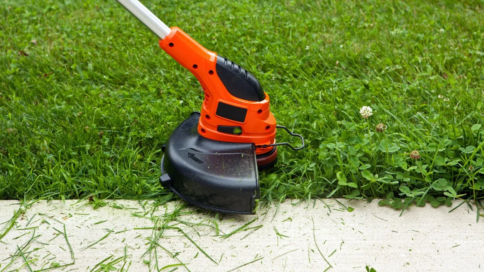 Orange and black grass trimmer cutting grass along the sidewalk.