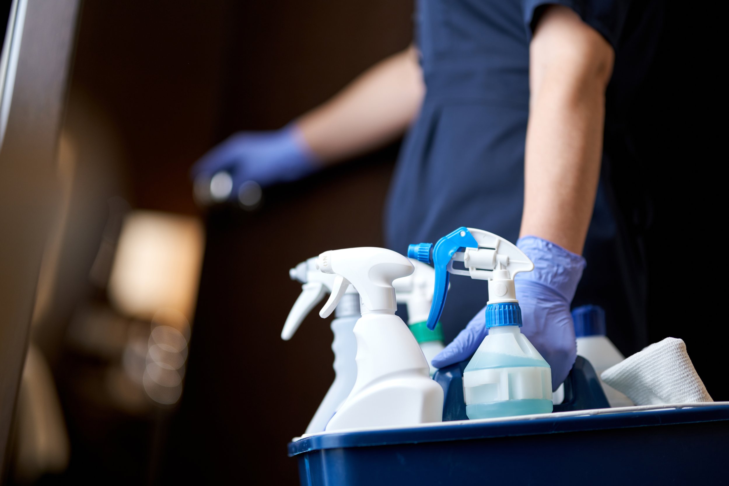 Person in gloves handling cleaning spray bottles in a professional cleaning setting.