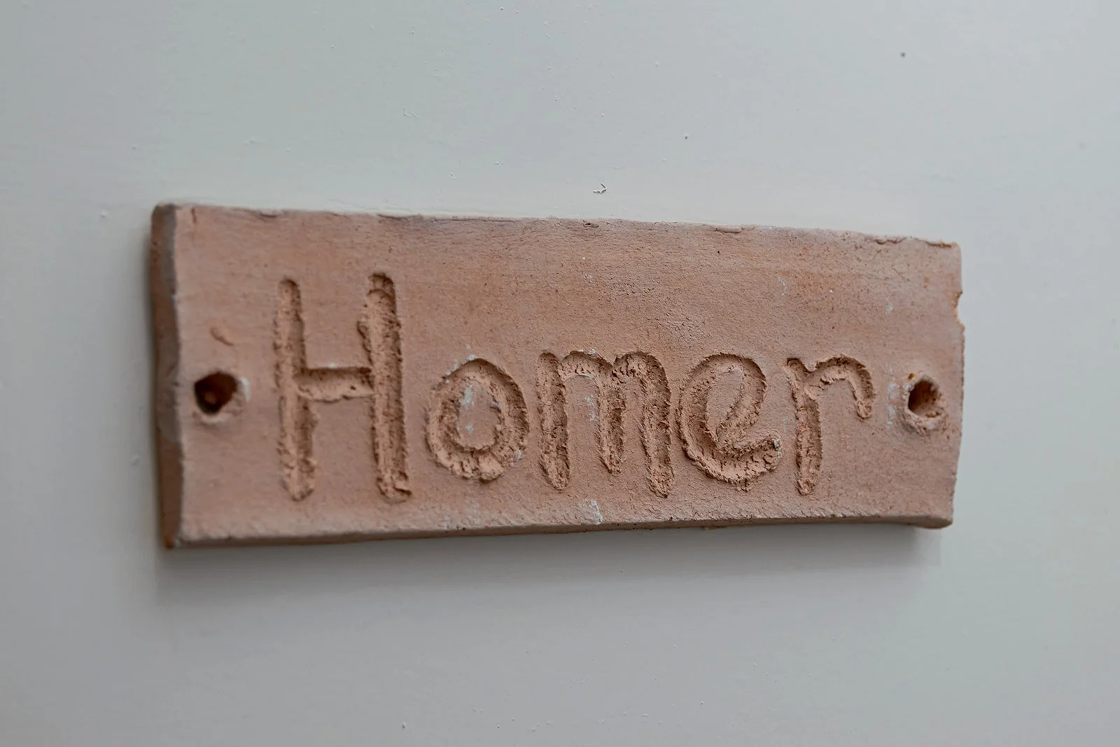 Close-up of a small, rectangular, pinkish-brown brick with the word 'Homer' engraved on it.