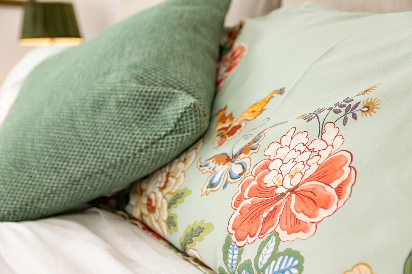 Close-up of a bed with a green textured pillow and a decorative pillow with floral and butterfly print.