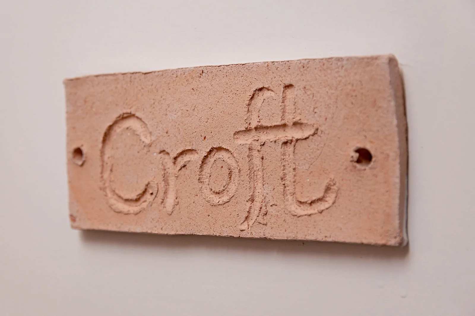 A pink rectangular brick with the word 'Croft' engraved on it, mounted on a white wall.