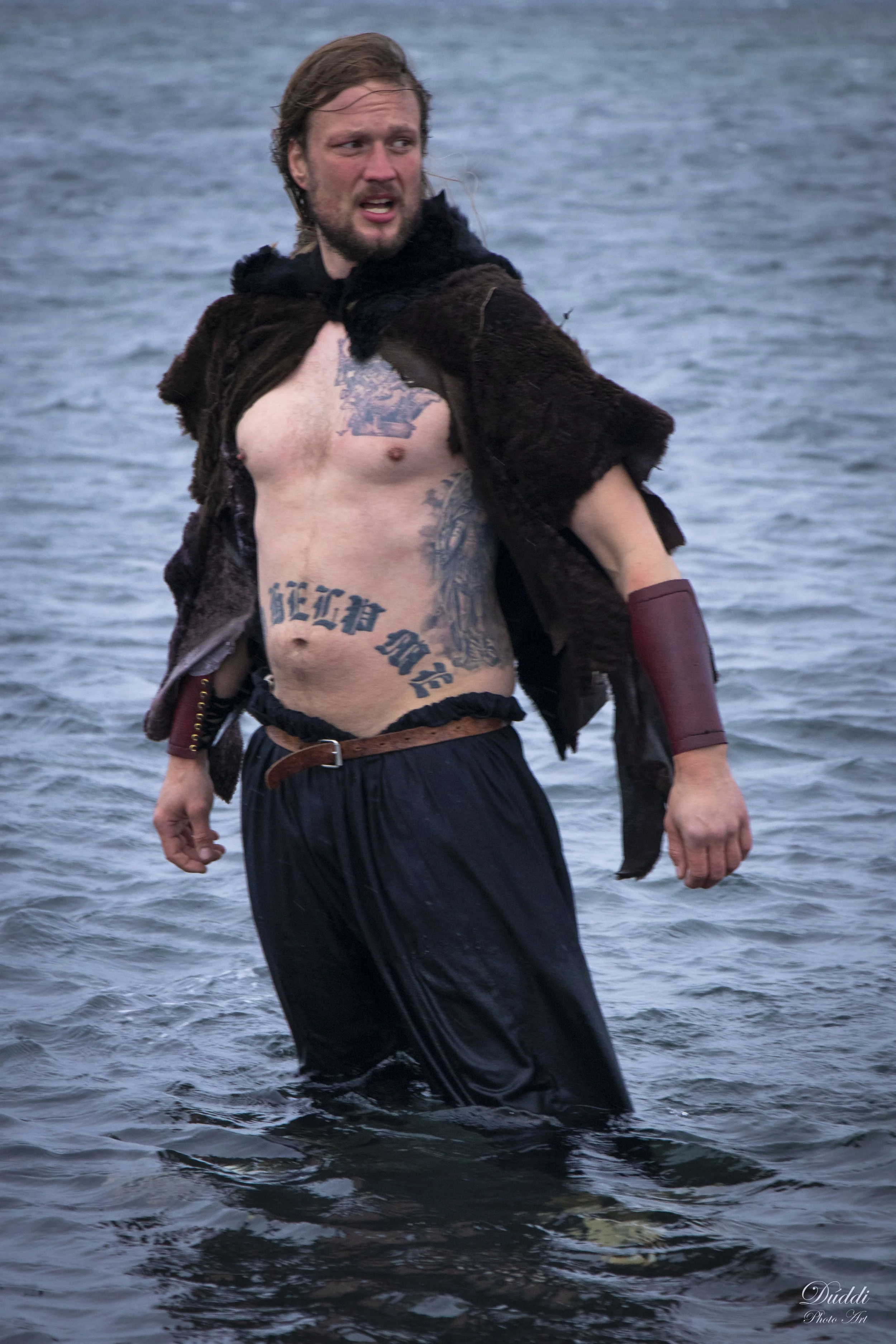 Viking with long hair and bierd stands in the sea.