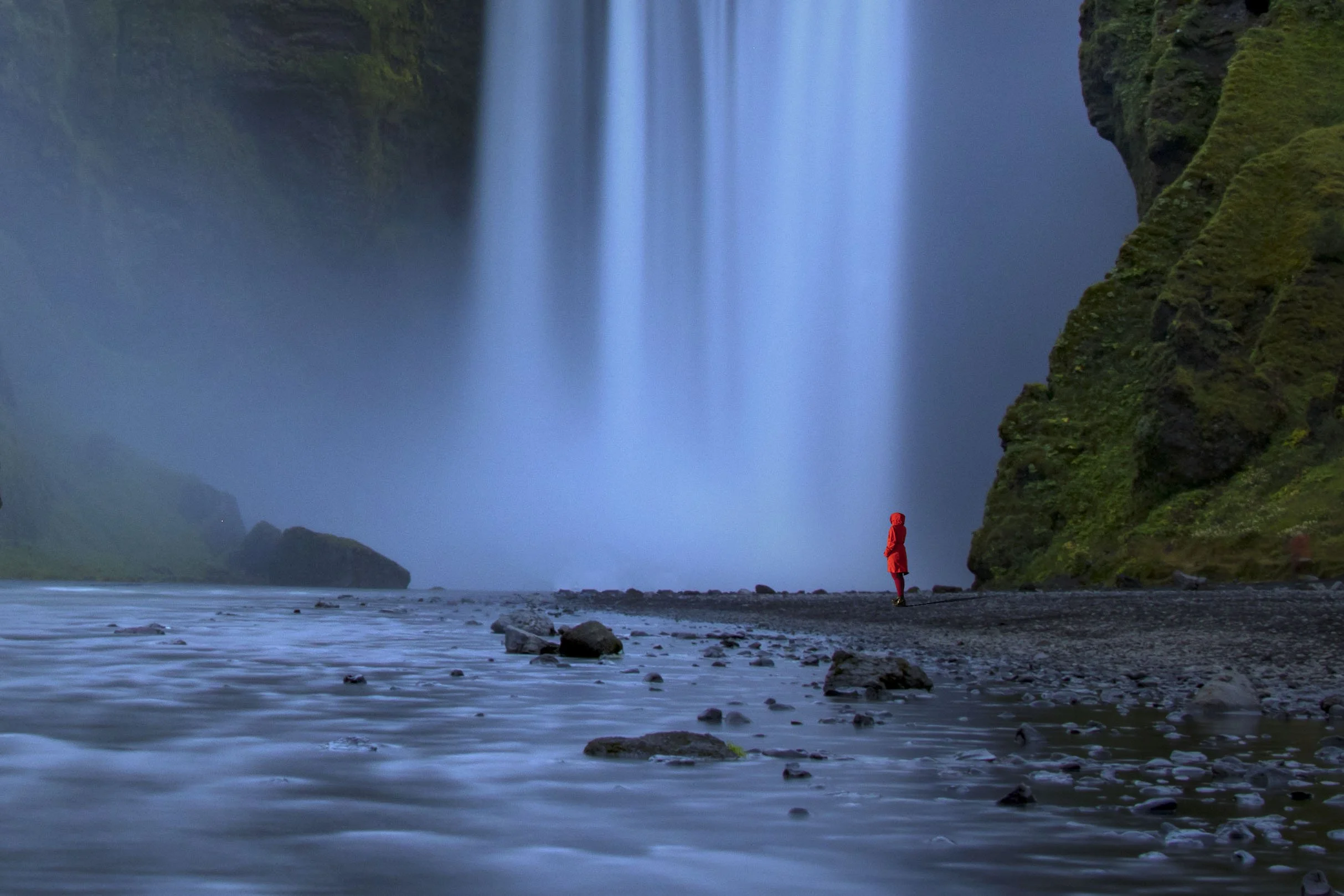 A woman, dressed in red, stands by Skógafoss in Iceland