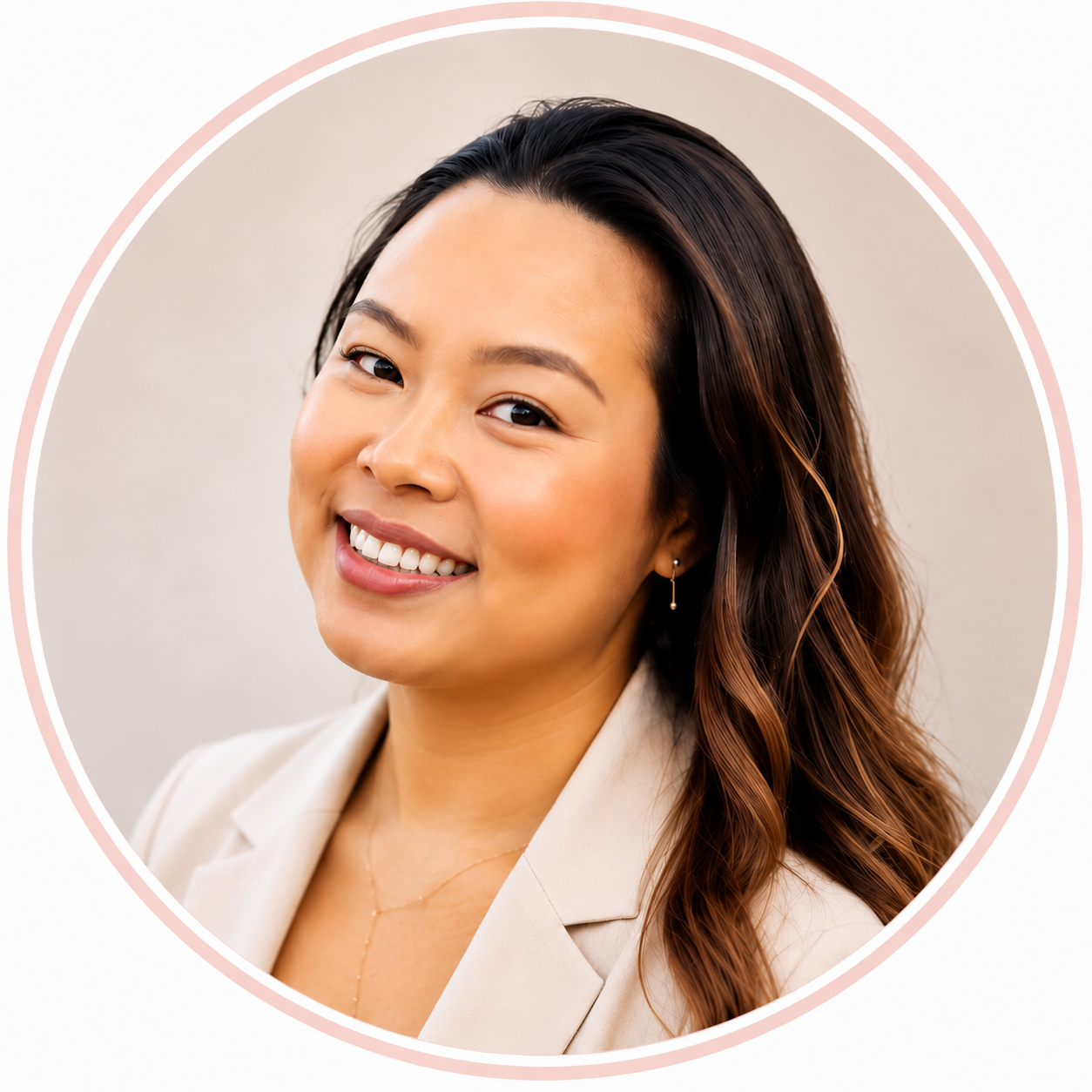 Close-up of a smiling woman with long wavy brown hair, wearing earrings and a beige blazer, against a neutral background.