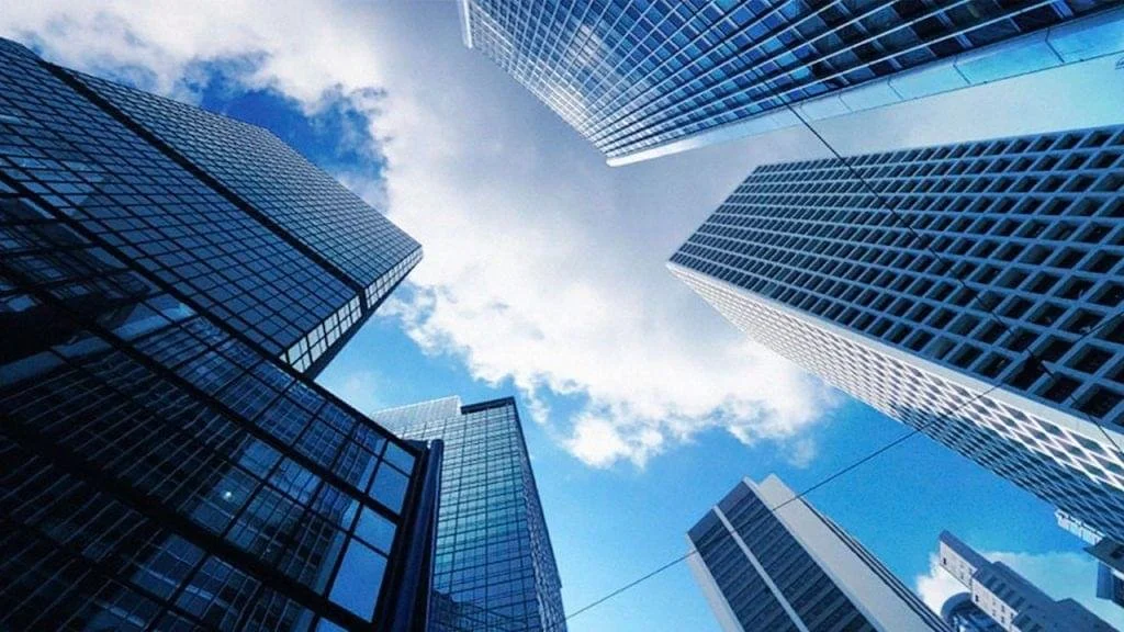 Vista aérea de rascacielos de vidrio en una ciudad moderna con cielo azul y nubes.