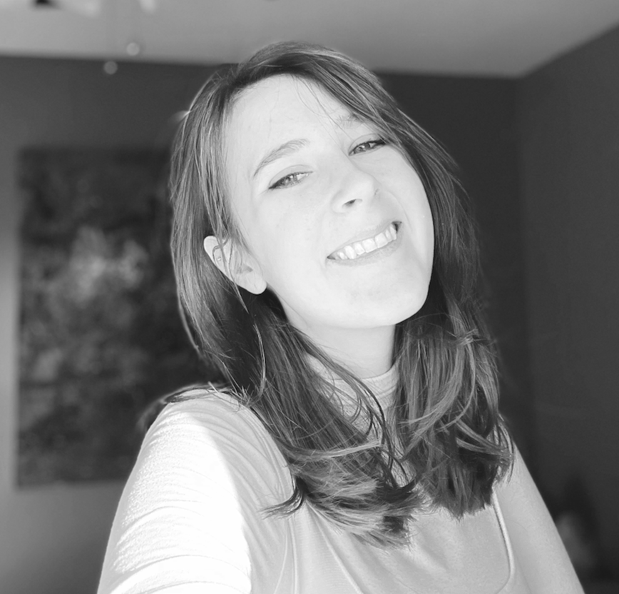 Black and white photo of a woman smiling, with shoulder-length hair, in an indoor setting.