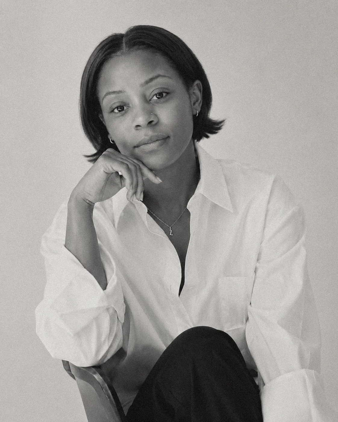 Black and white portrait of a woman with short hair, wearing a white shirt, sitting and resting her chin on her hand.