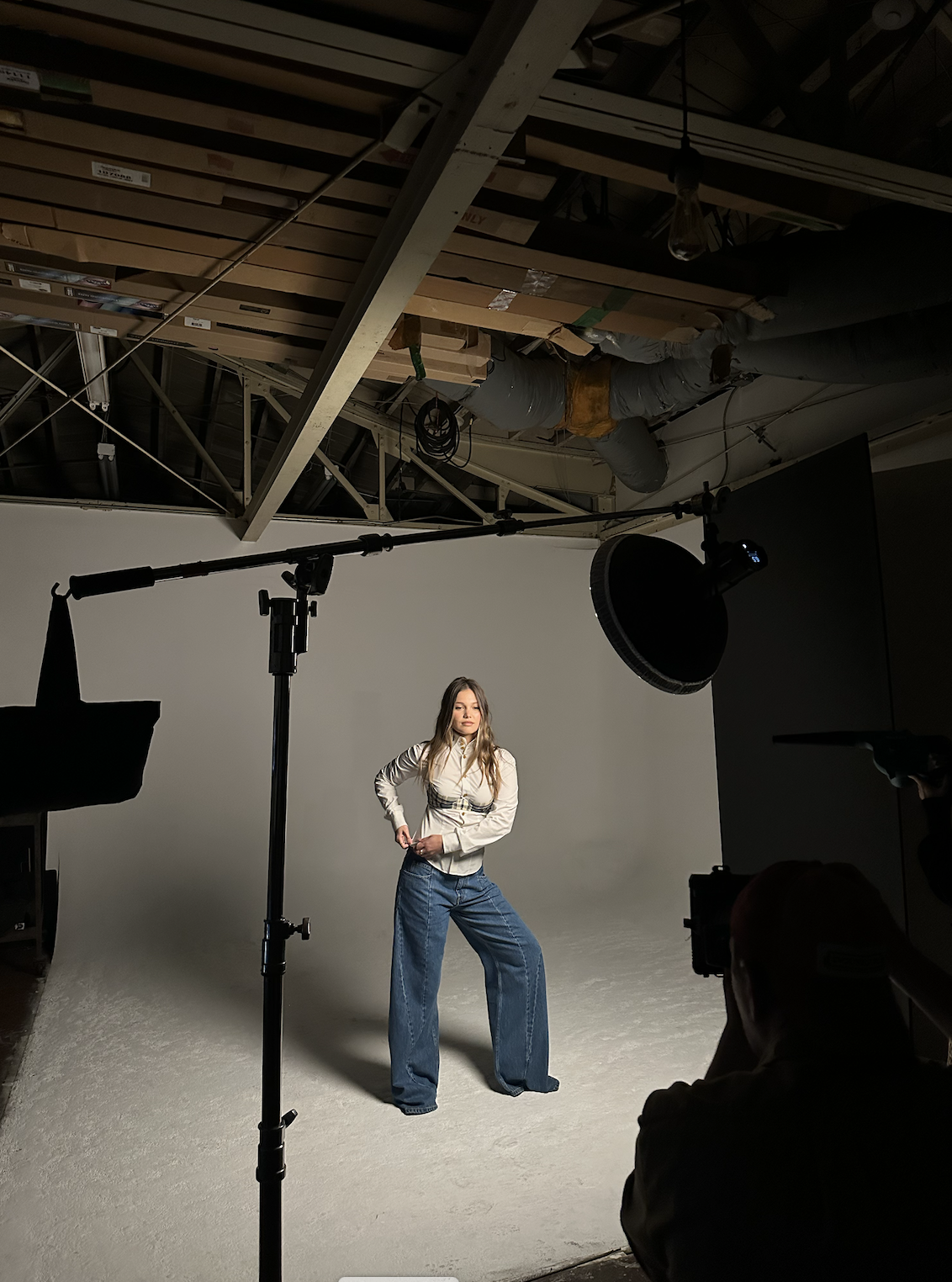 A young woman posing in a photo studio with professional lighting and equipment, in front of a plain white backdrop.