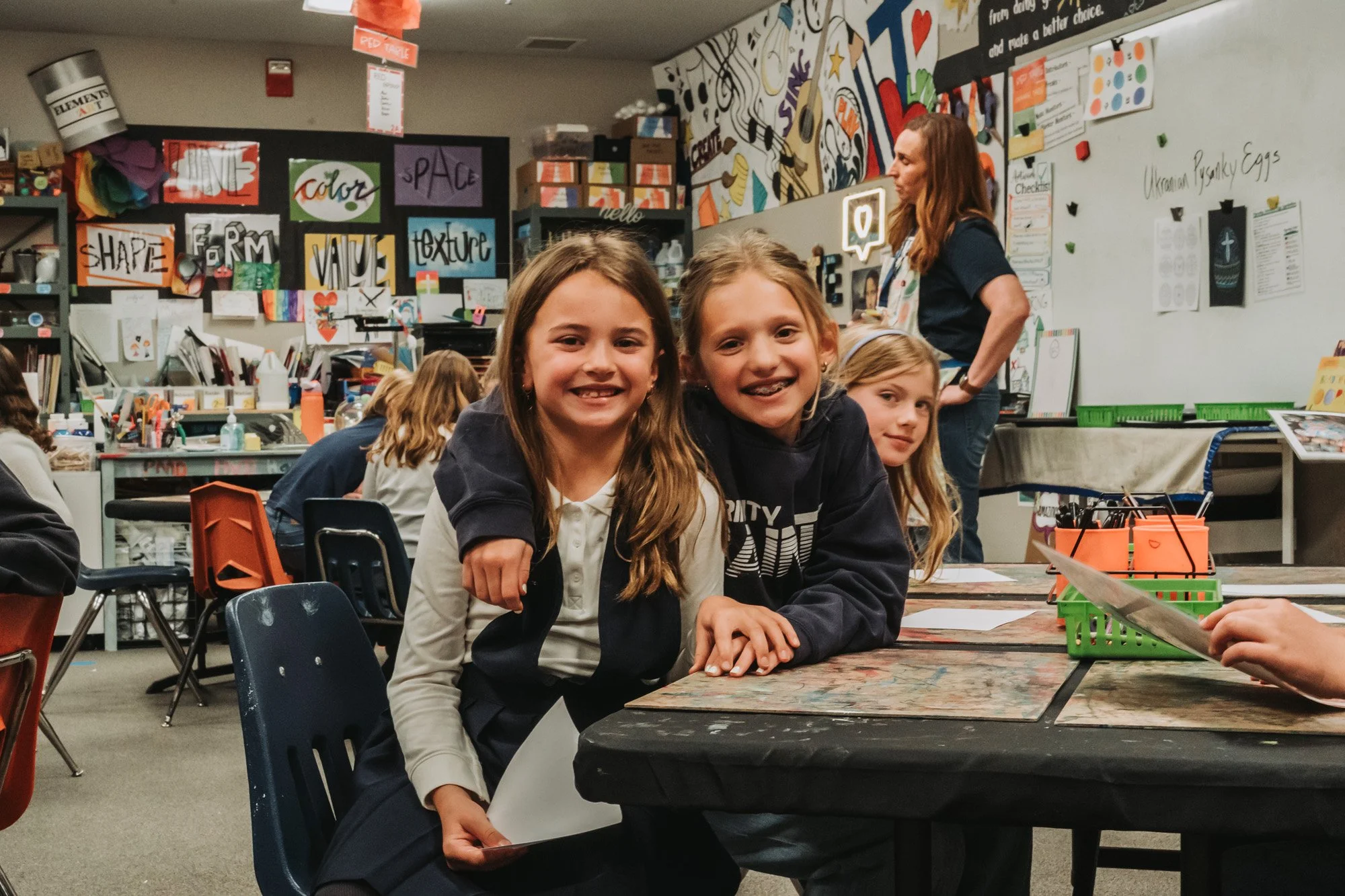 Three young students smiling at a craft table in the art room