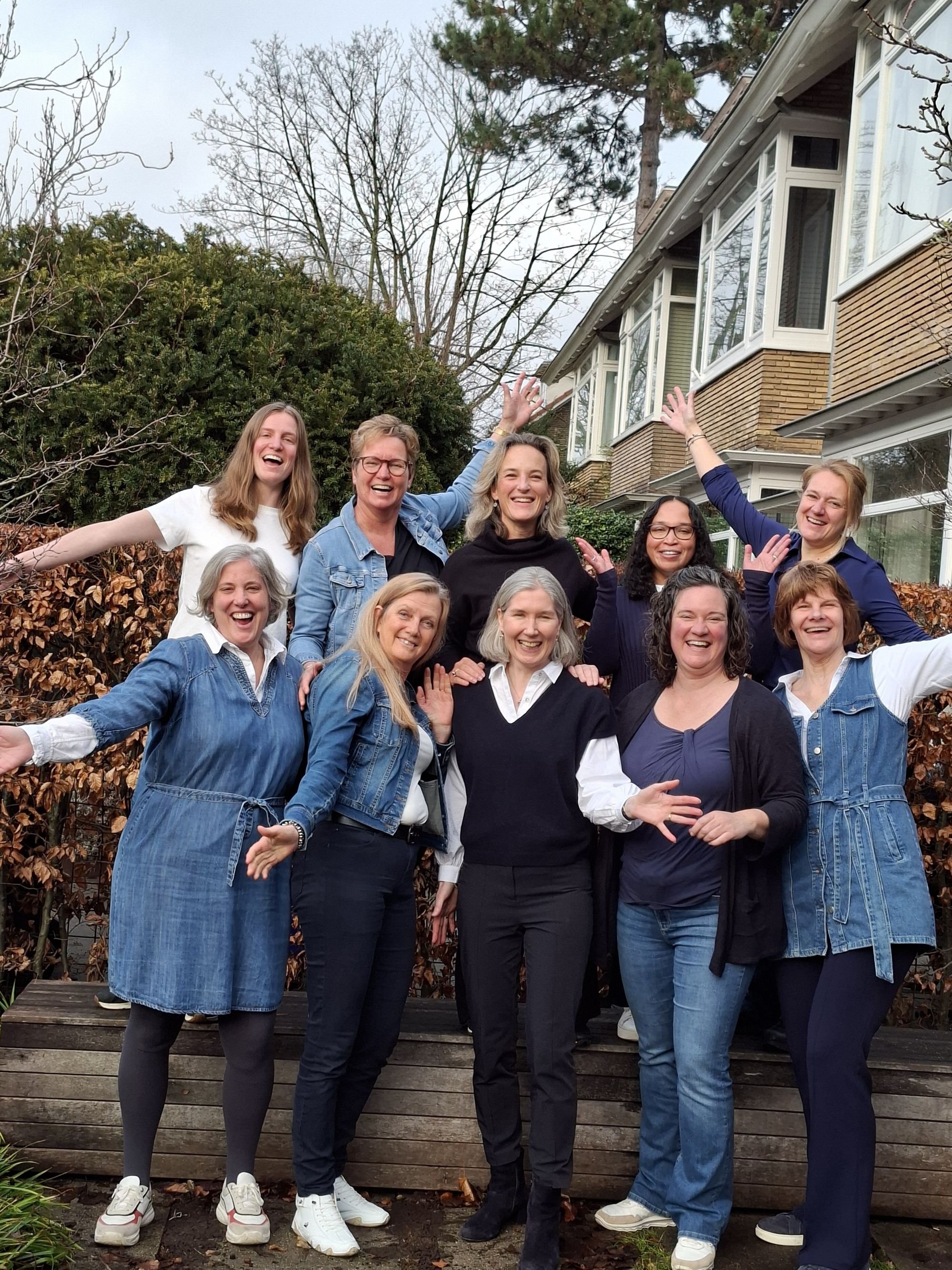 Een group vrouwen gekleed in wit en spijkerstof, lacht naar de camera.