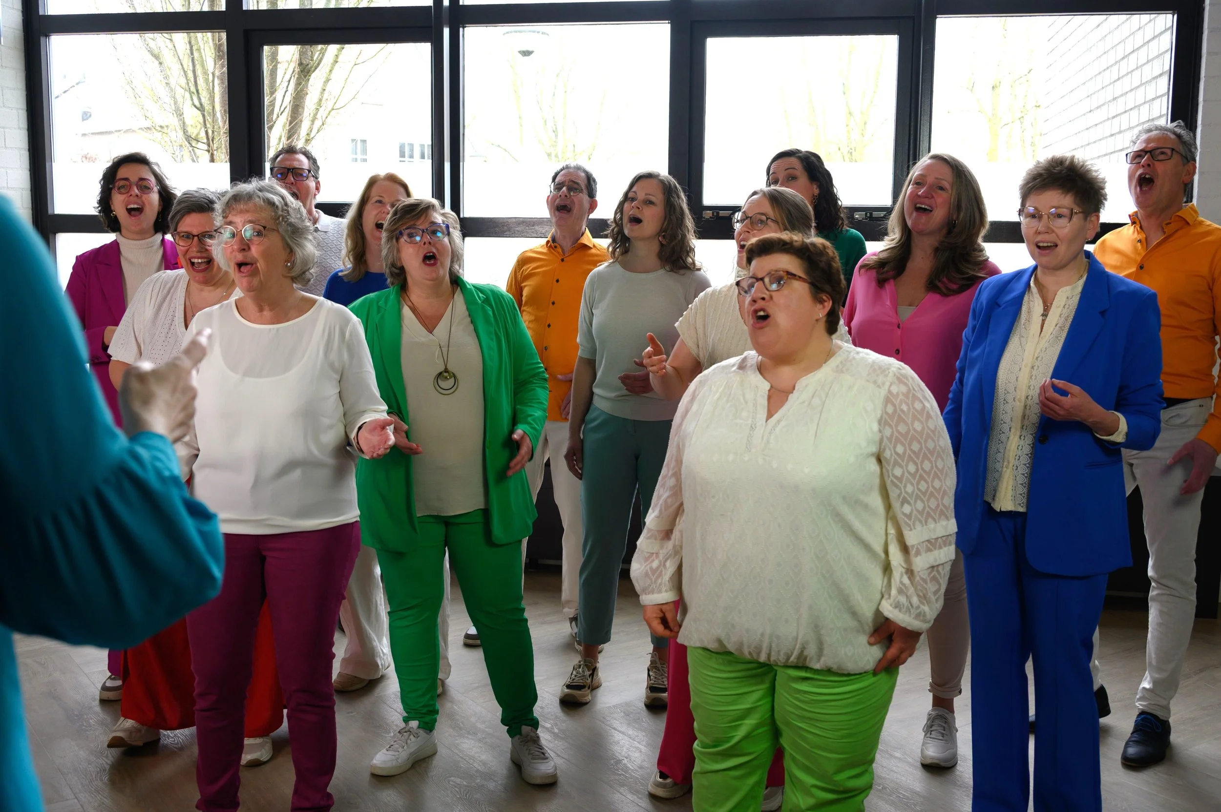 Een groep mensen, gekleed in felle kleuren, zingt samen.