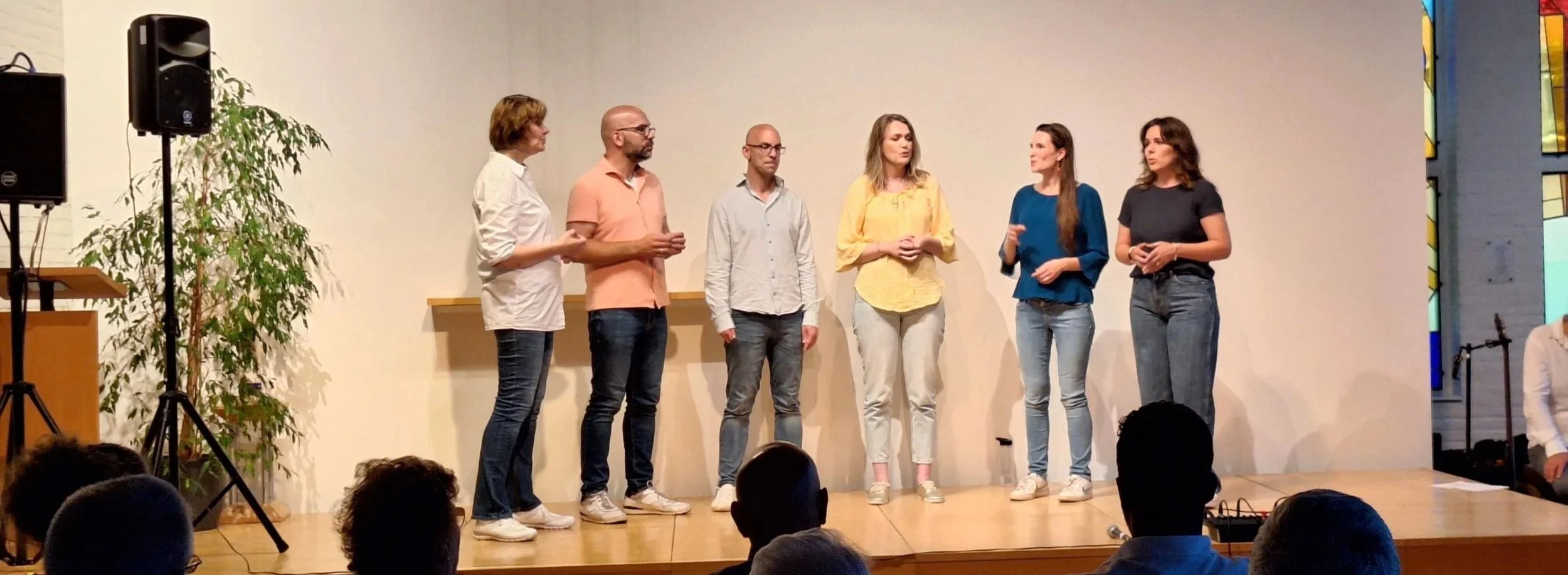 Zes mensen staan op een podium en zingen samen.