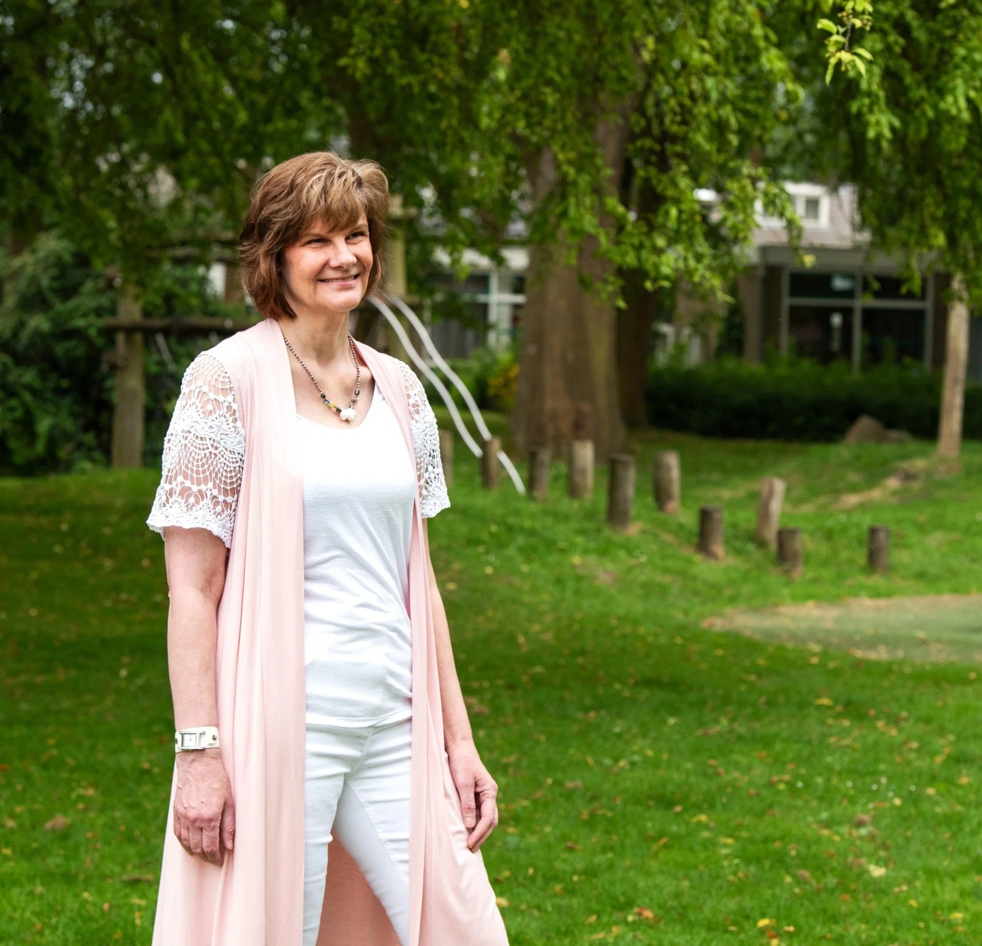 Een vrouw met een wit shirt en een zacht roze vest lacht.