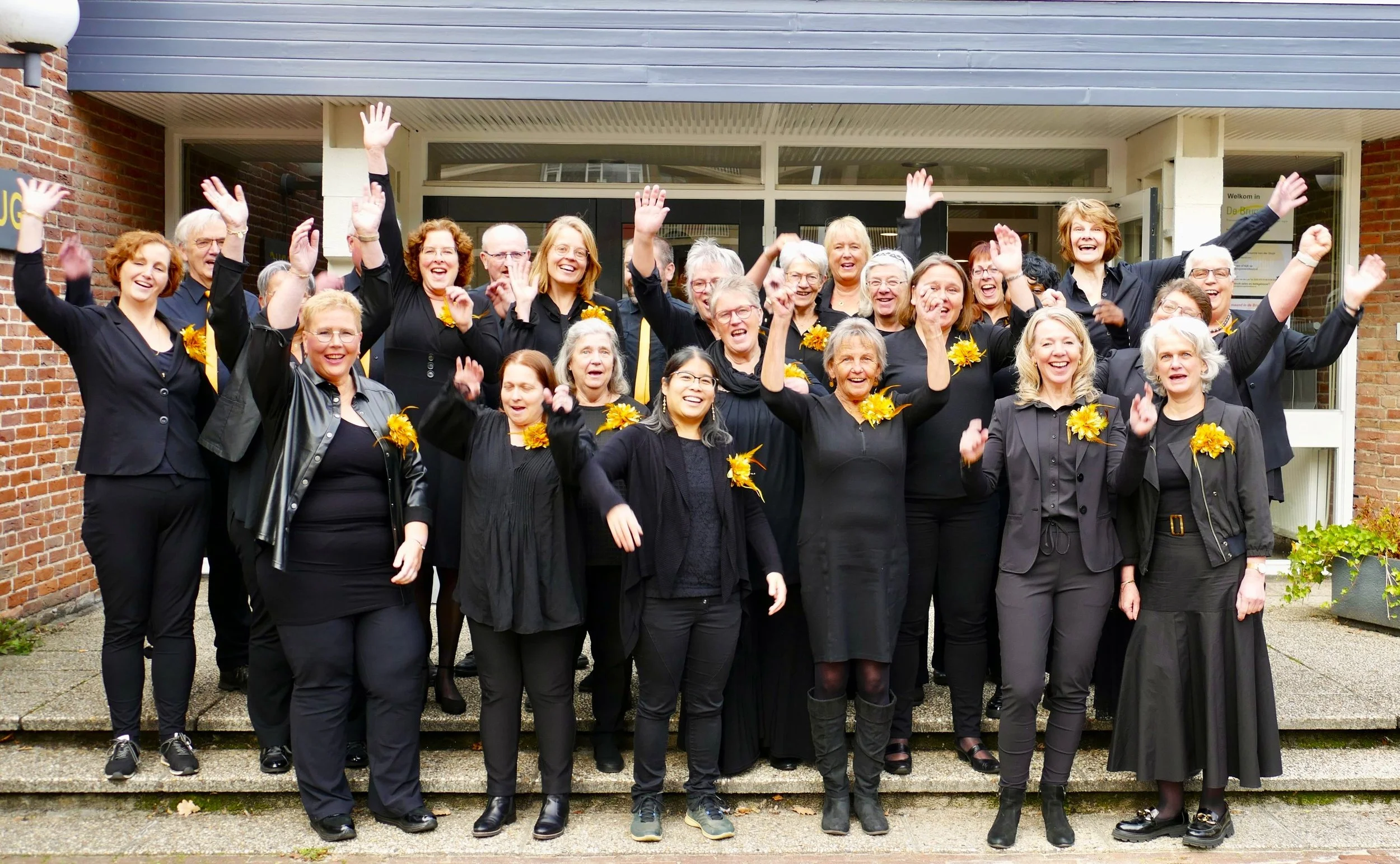 Een groep mensen, gekleed in het zwart, die lachen en zwaaien naar de camera.