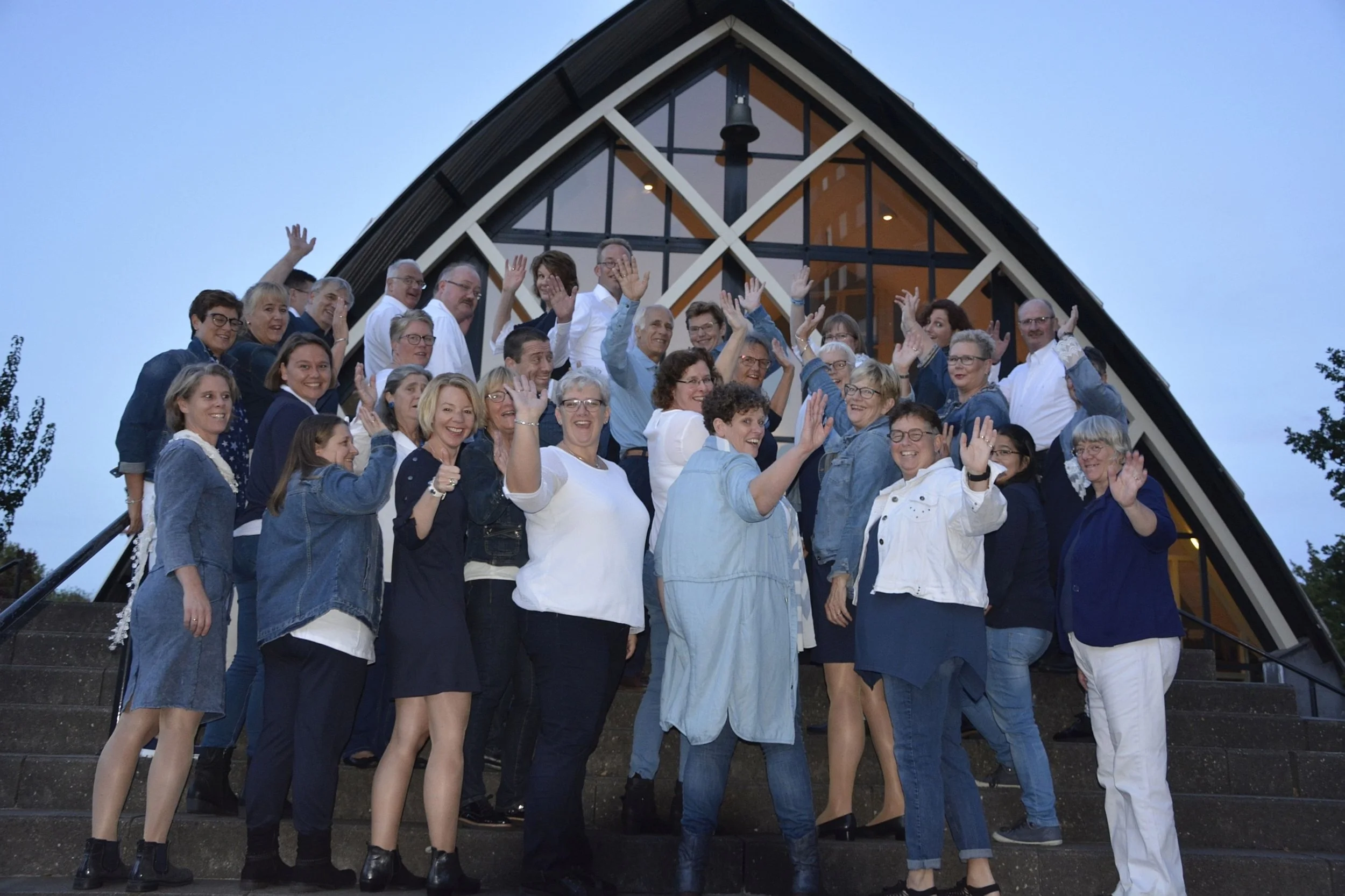 Een grote groep mensen kijkt achterom en zwaait naar de camera.