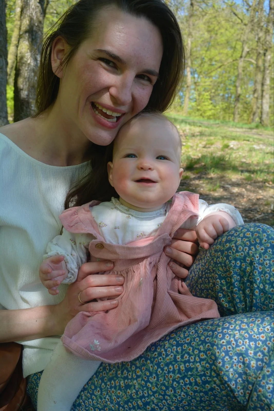 Een jonge vrouw houdt een baby vast in een zacht roze jurkje. Ze lachen allebei. 