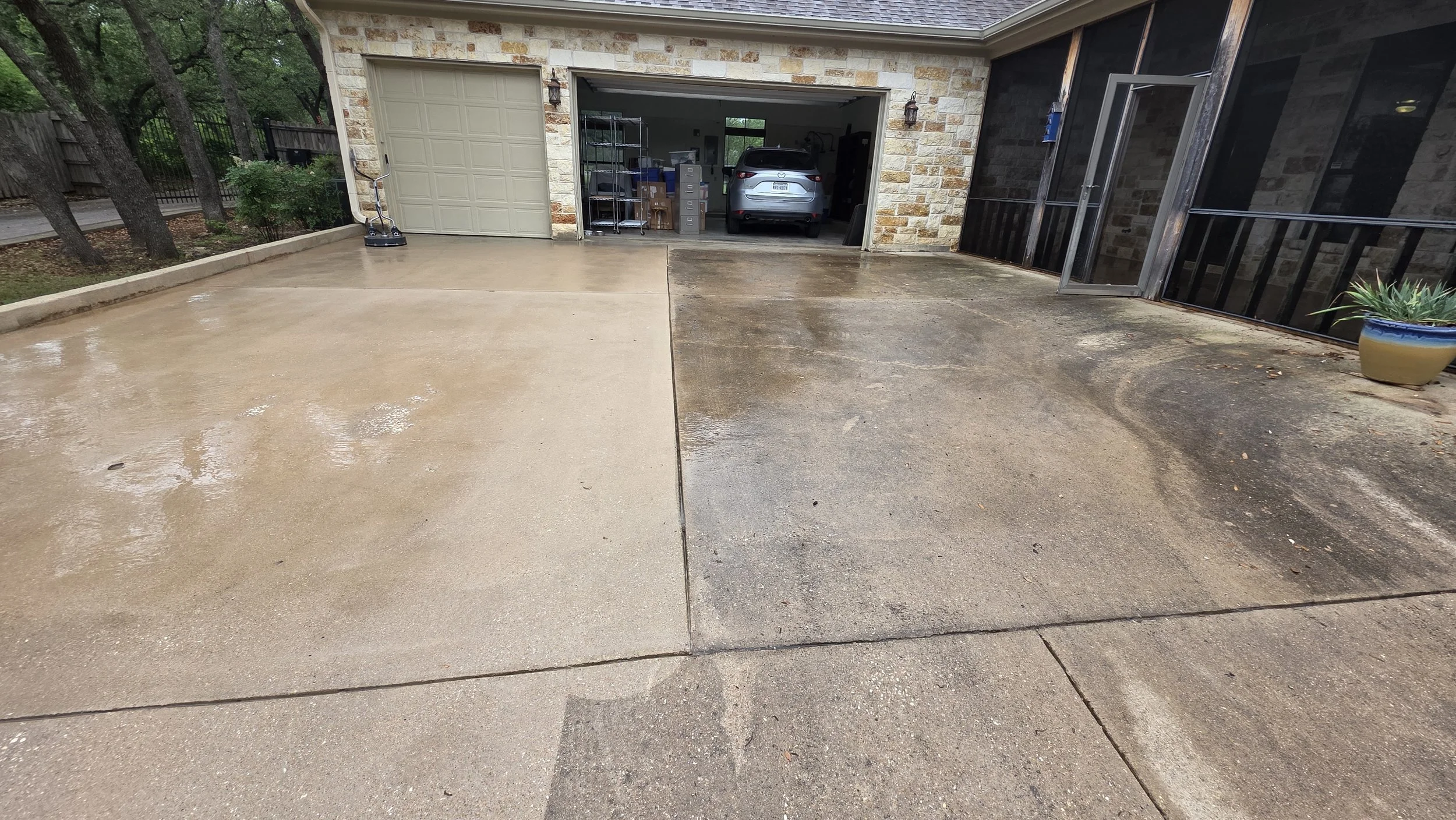 Photo of a driveway with one side clean and wet, the other side dirtier and covered with leaves and debris. A garage with a car inside and various storage items is visible in the background.